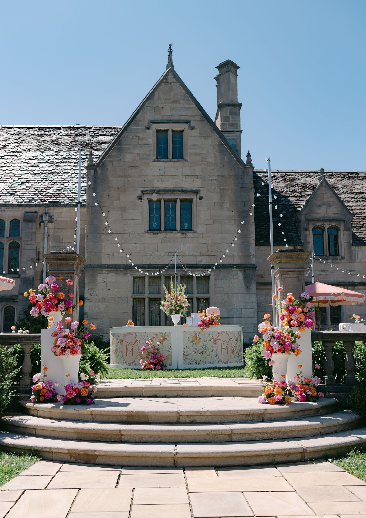 Outdoor wedding ceremony setup at Hartwood Acres with colorful floral arrangements and string lights under blue sky.