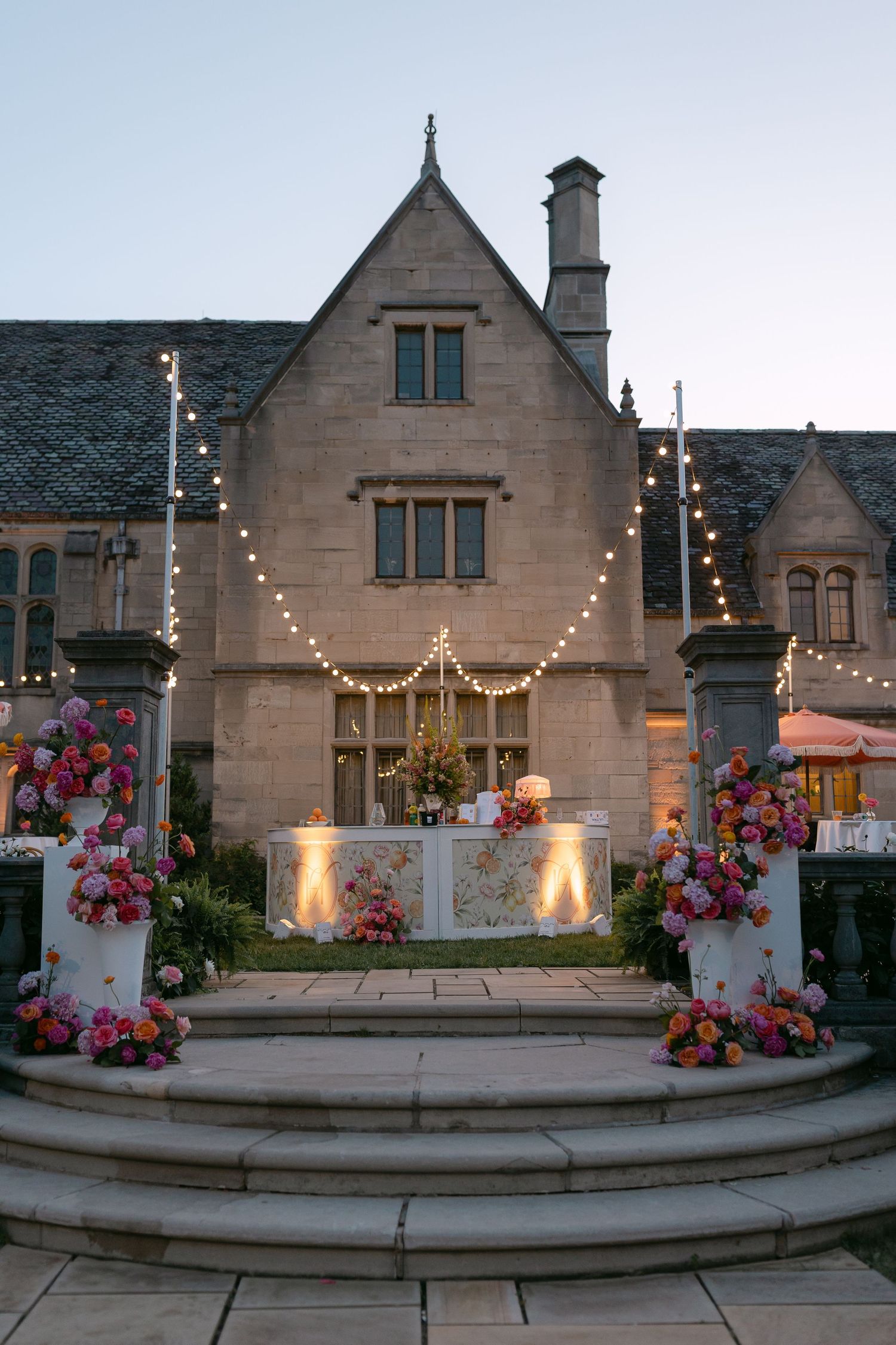 Stunning twilight wedding reception setup at stone manor with string lights, floral bar, and large letter arrangements.