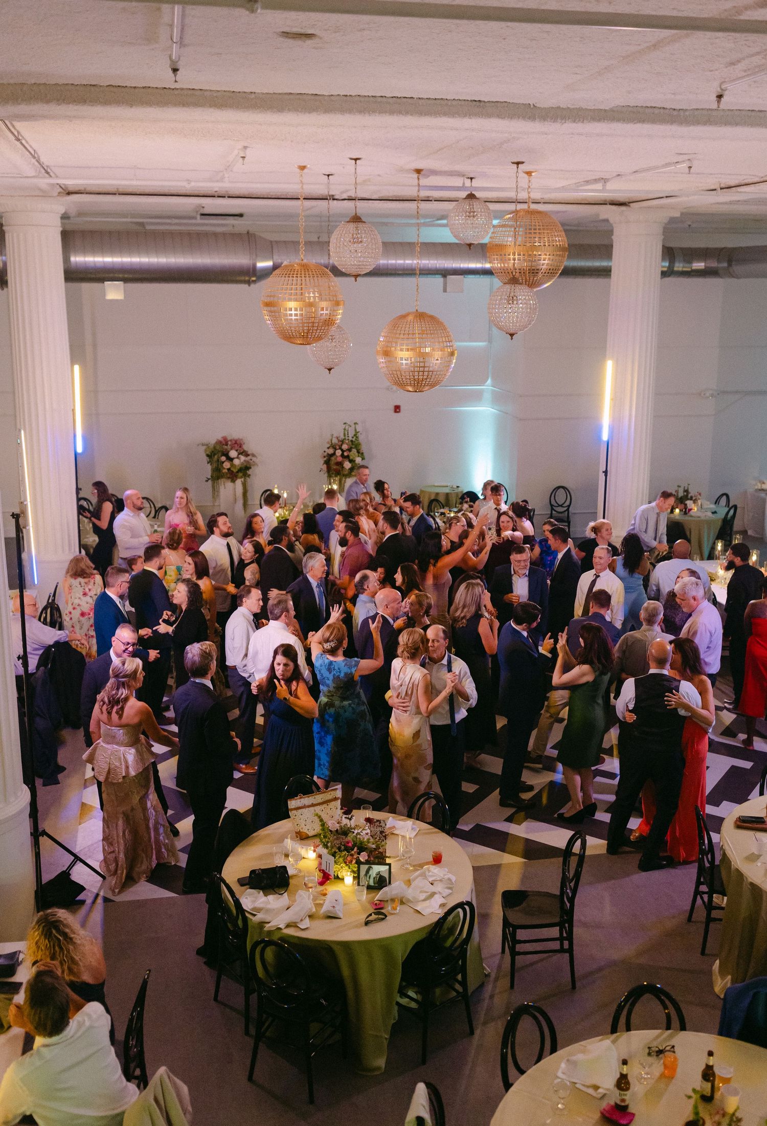 Elegant wedding reception with guests dancing under gold globe pendant lights in a spacious venue.