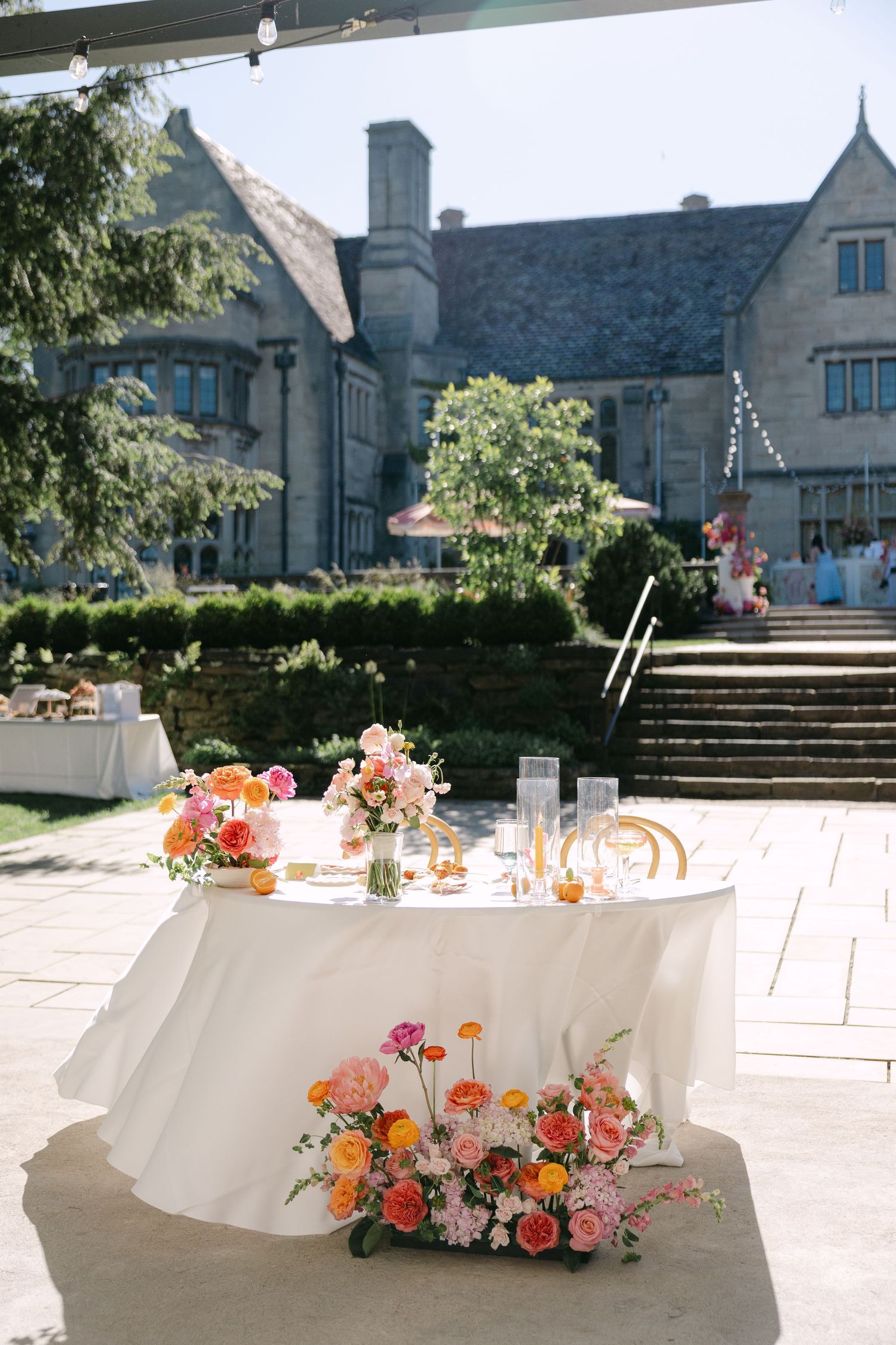 Sweetheart table with white linen and colorful floral arrangements in front of stone mansion.
