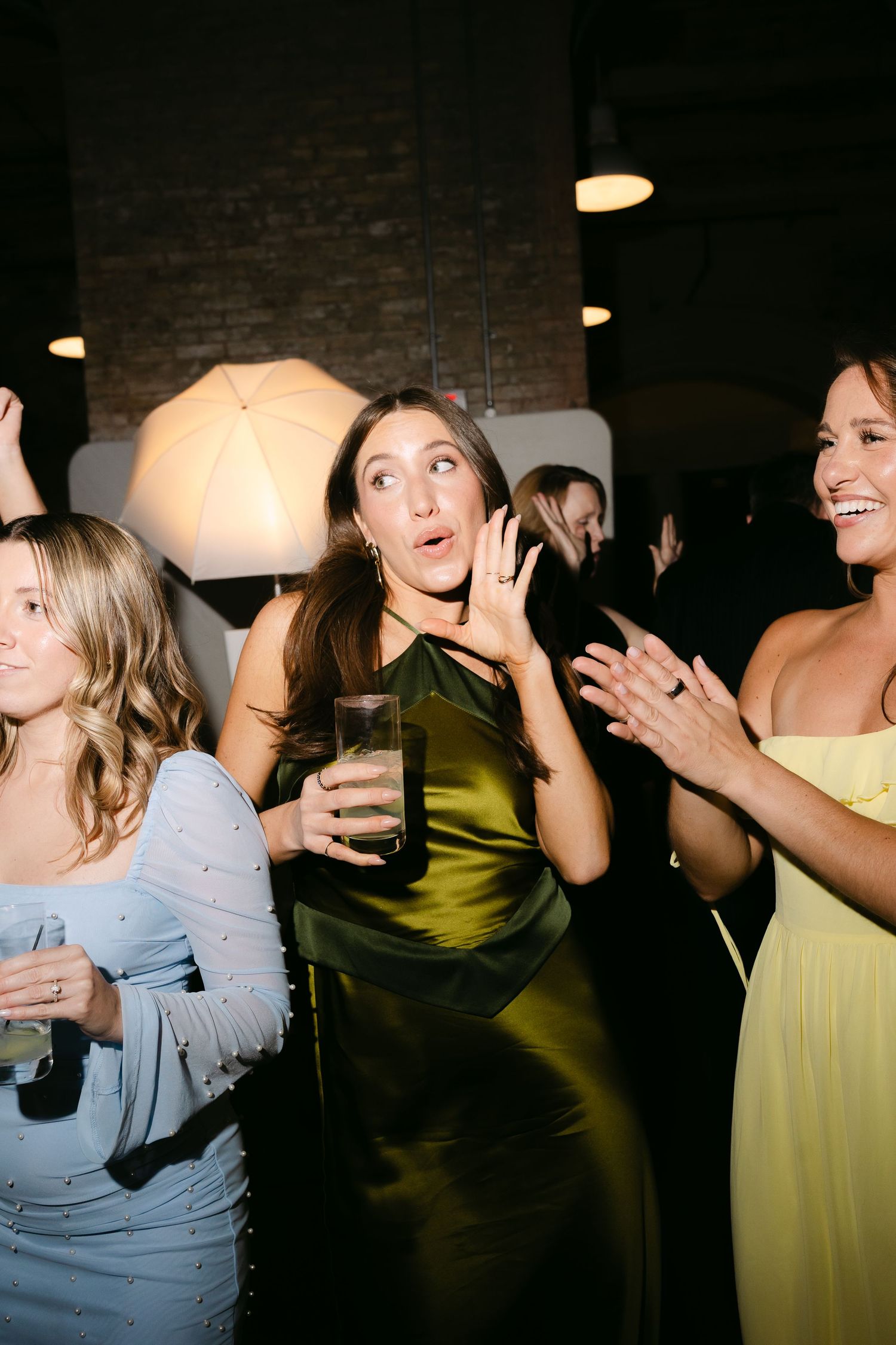 Woman in olive green dress looking surprised while dancing with friends at a wedding reception.