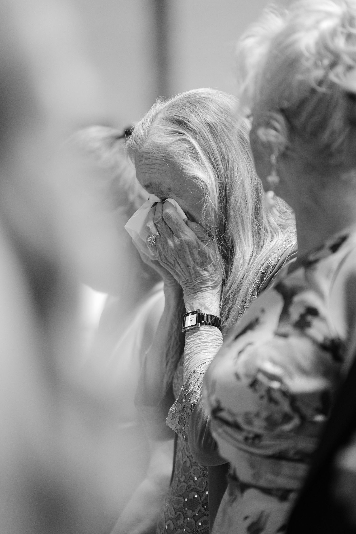 Elderly woman wiping tears with tissue at emotional event, black and white photo.