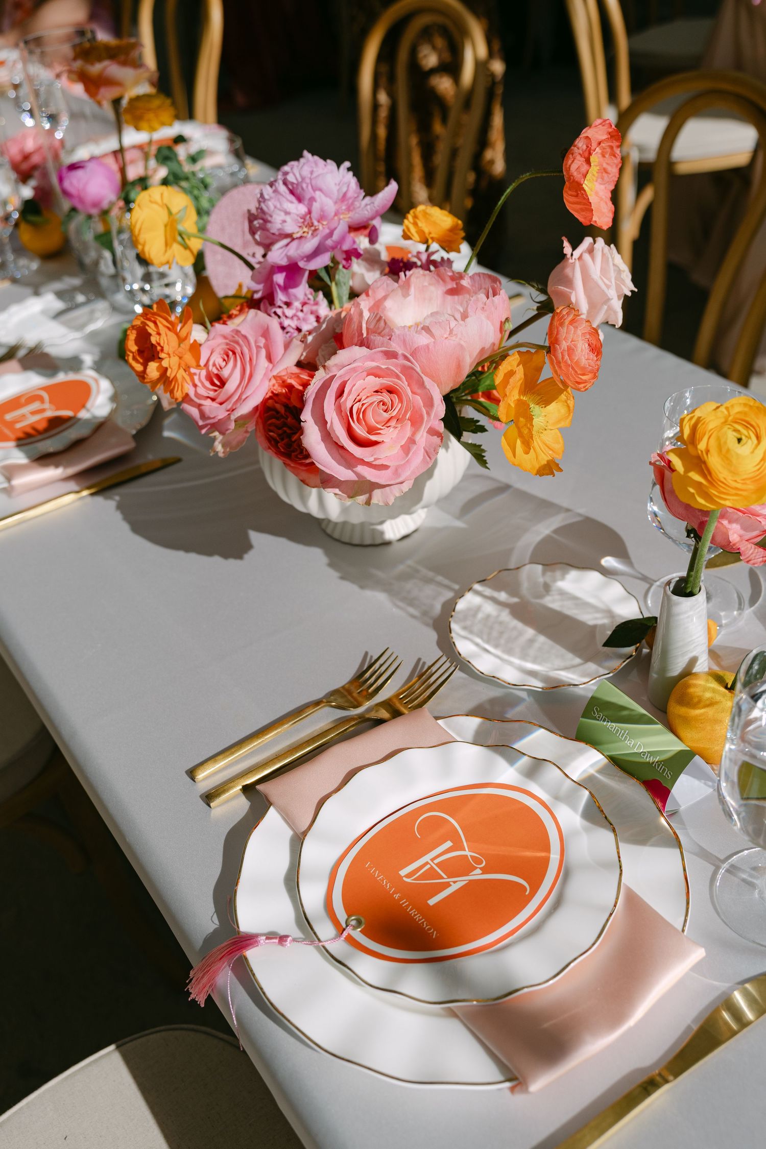 Elegant wedding table setting with pink and orange floral centerpieces and gold cutlery.