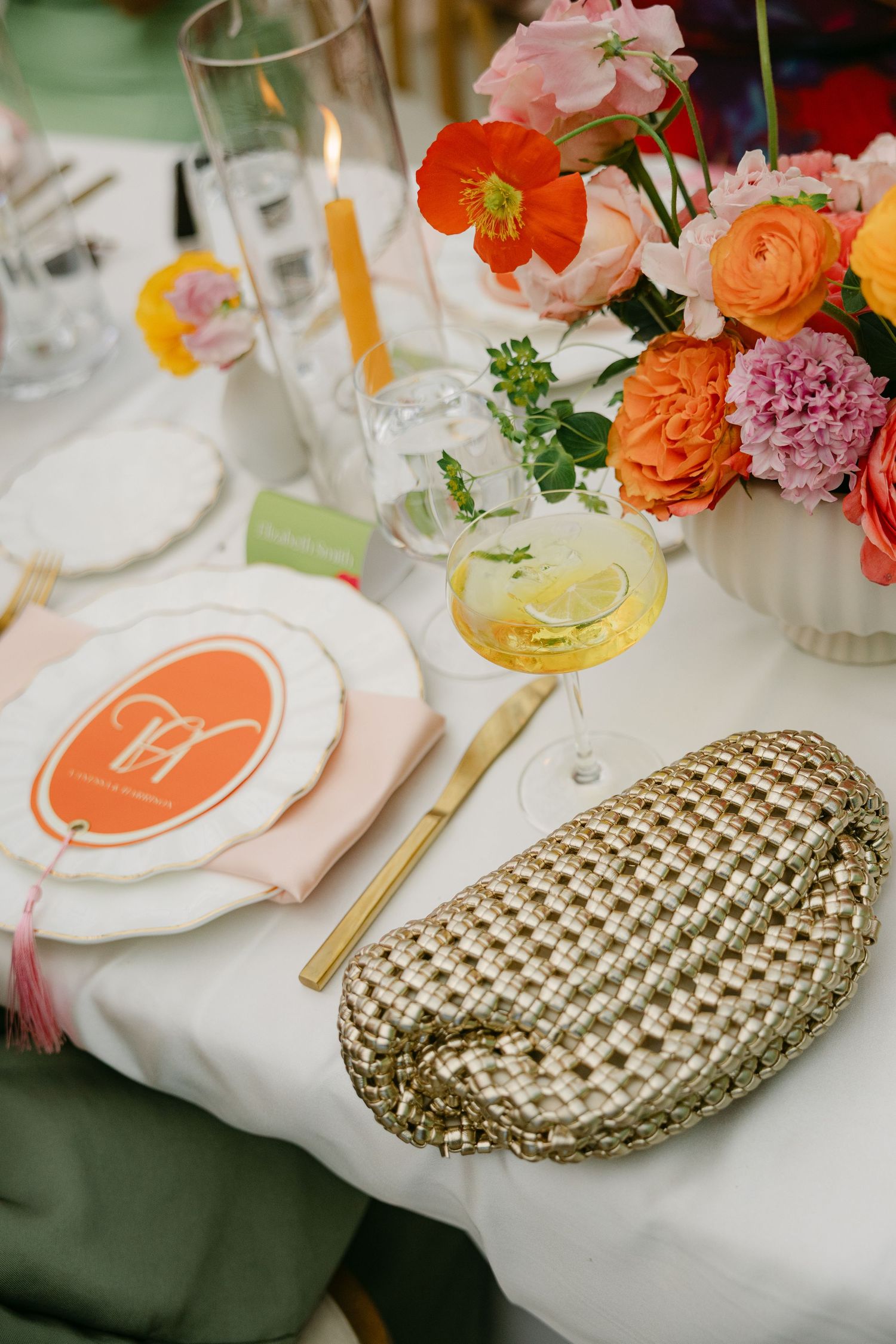 Elegant wedding table setting with orange and pink flowers, gold cutlery, and citrus cocktail garnish.