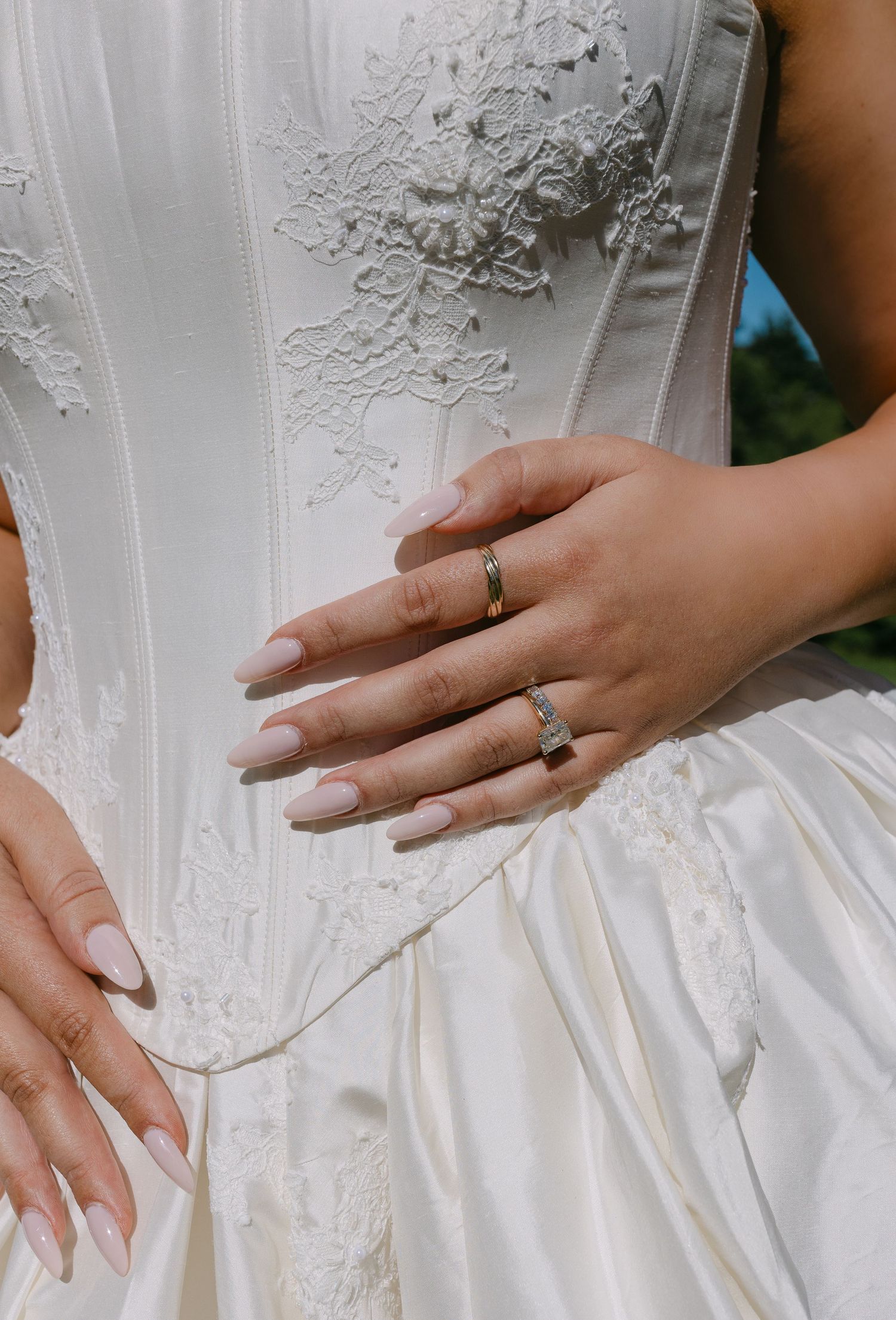 Close-up of bride's hands with wedding rings resting on white lace corset wedding gown.