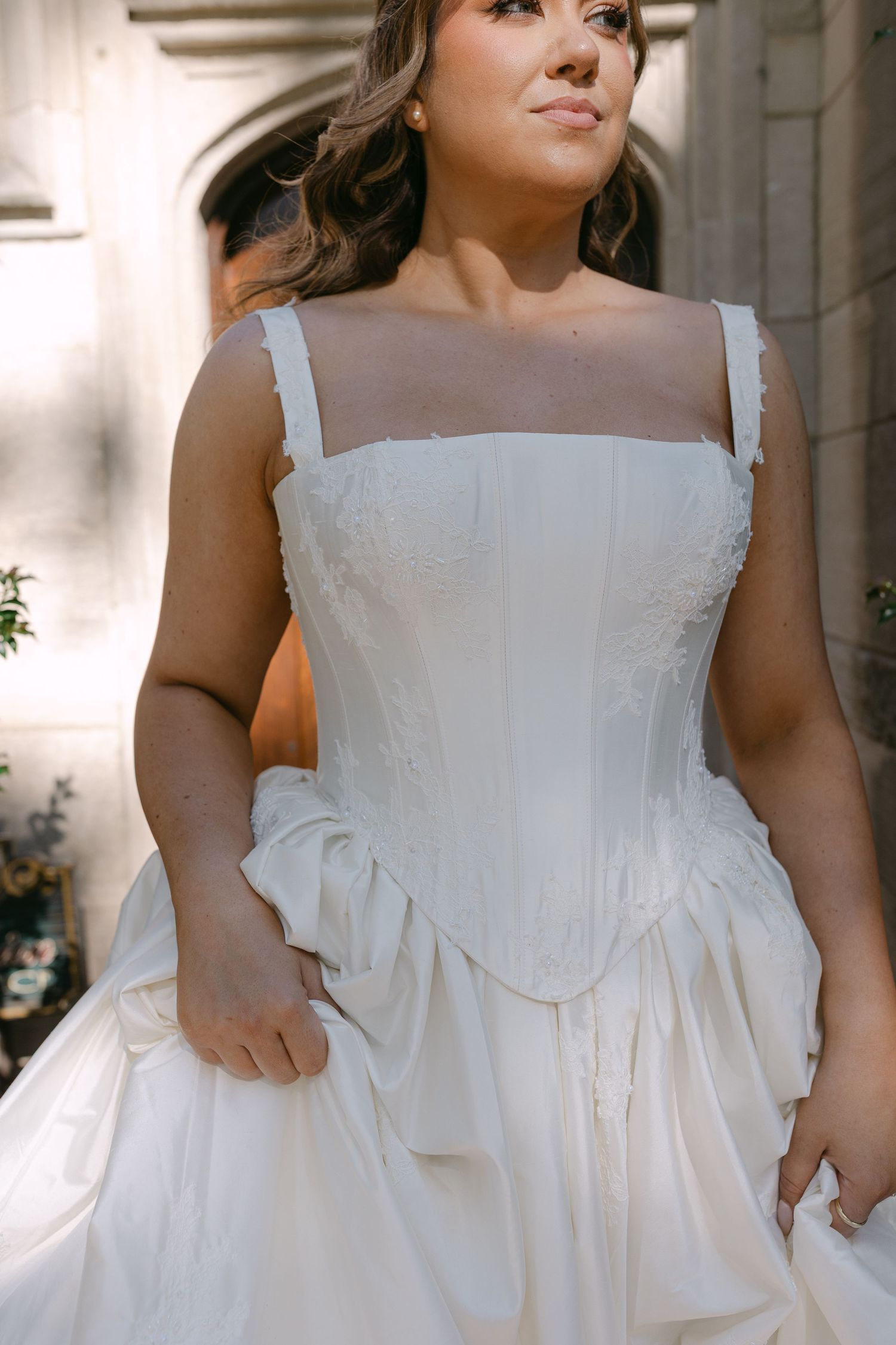 Close-up of a bride in a white corset wedding gown with sheer straps and floral embroidery details.