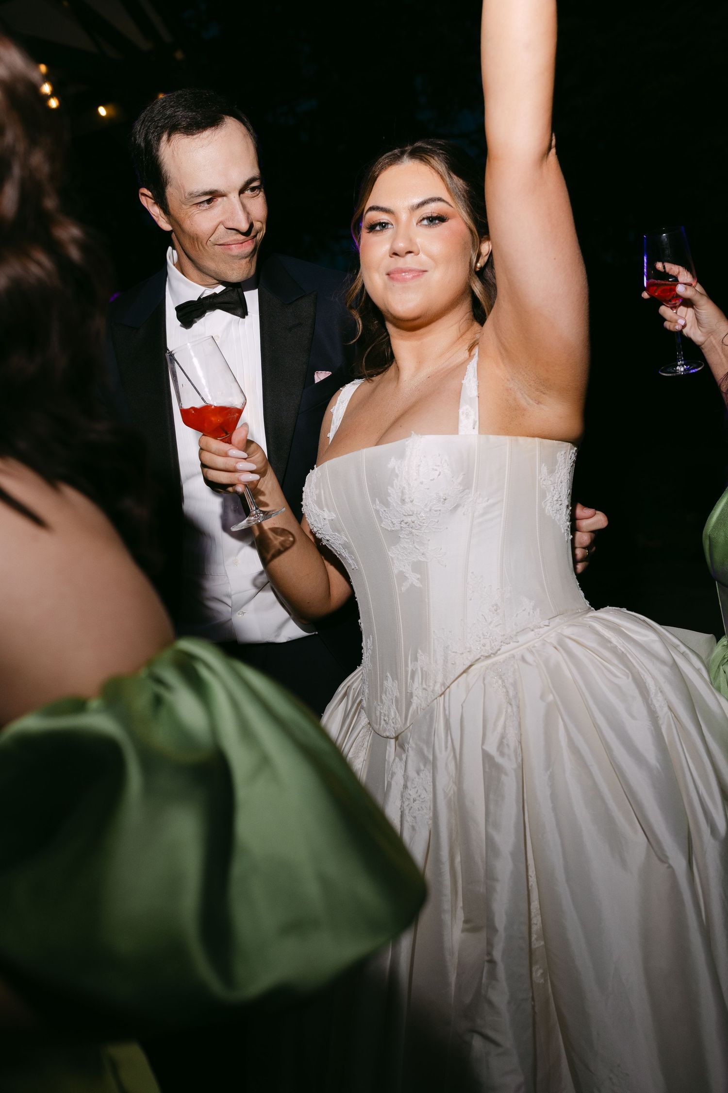 Bride in white corset gown celebrates with groom in tuxedo at wedding reception dance floor.