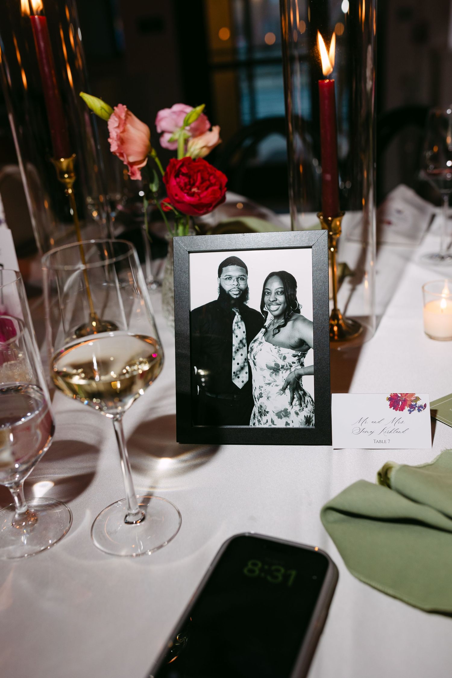 Black and white framed wedding photo displayed on reception table with wine glasses, candles, and floral centerpiece.