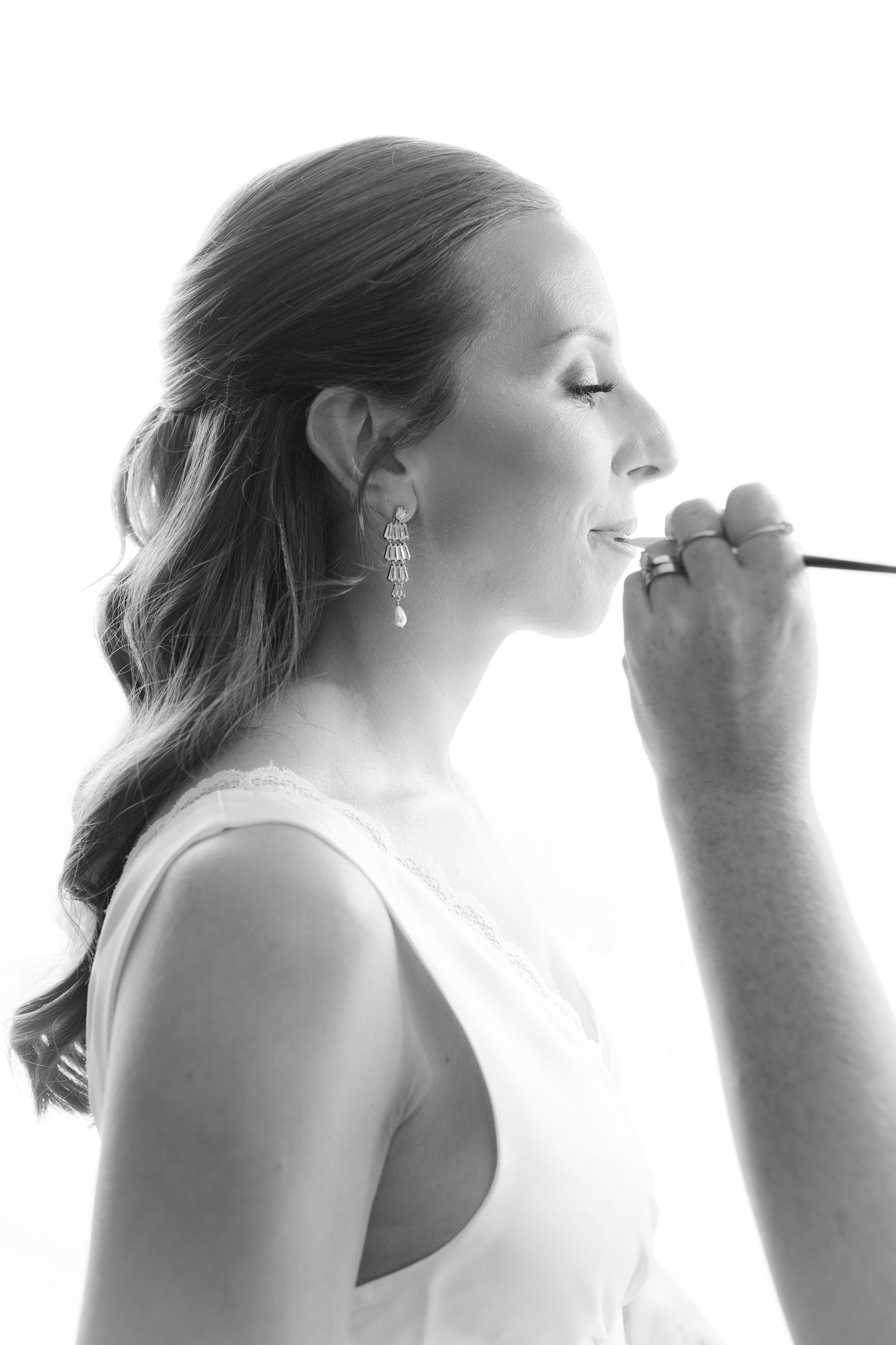 Black and white portrait of a bride having lipstick applied during wedding day preparations.