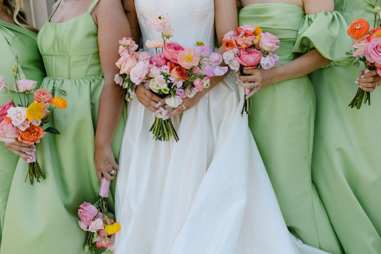 Bride in white gown surrounded by bridesmaids in mint green dresses, all holding vibrant pink and orange floral bouquets.