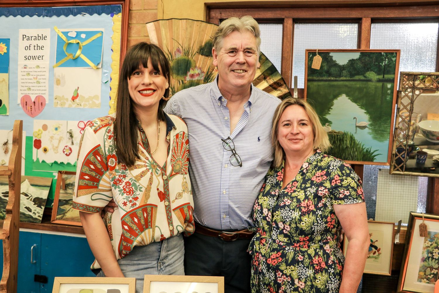 Three people pose together in front of colorful artwork displays in a school or gallery setting.
