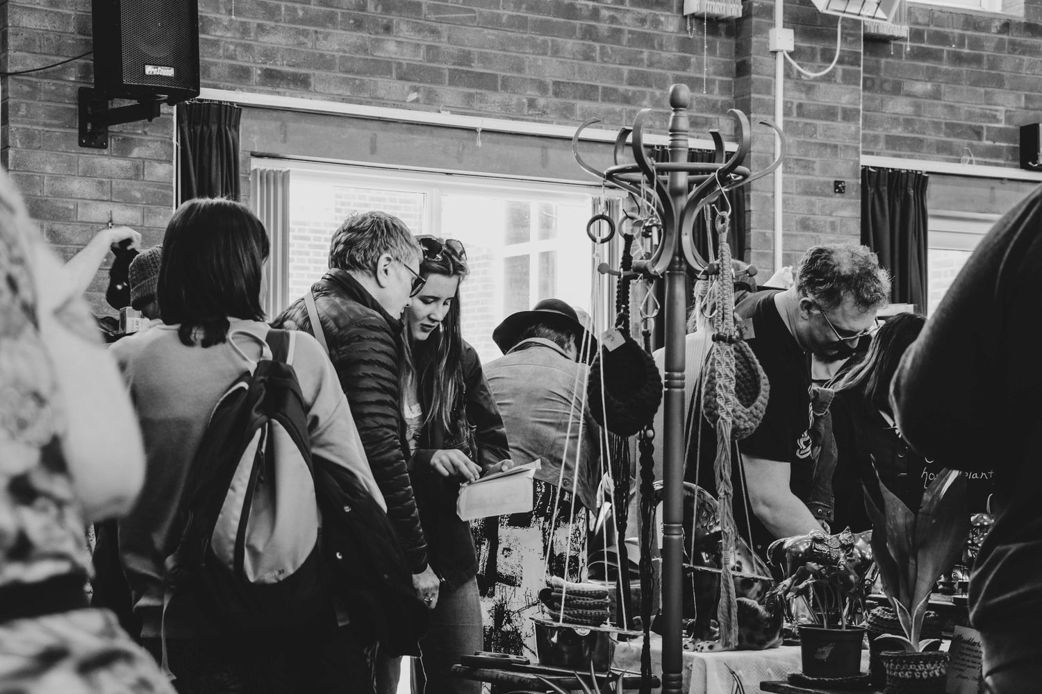 Black and white photo of crowd gathering around ski equipment outside brick building.