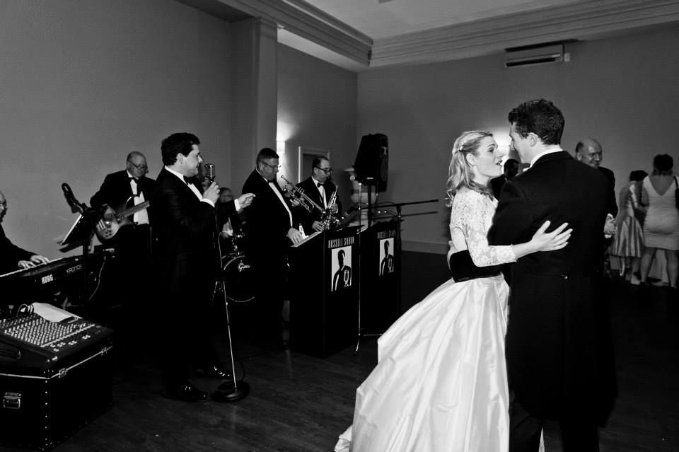 Black and white wedding reception photo with band playing as couple dances.