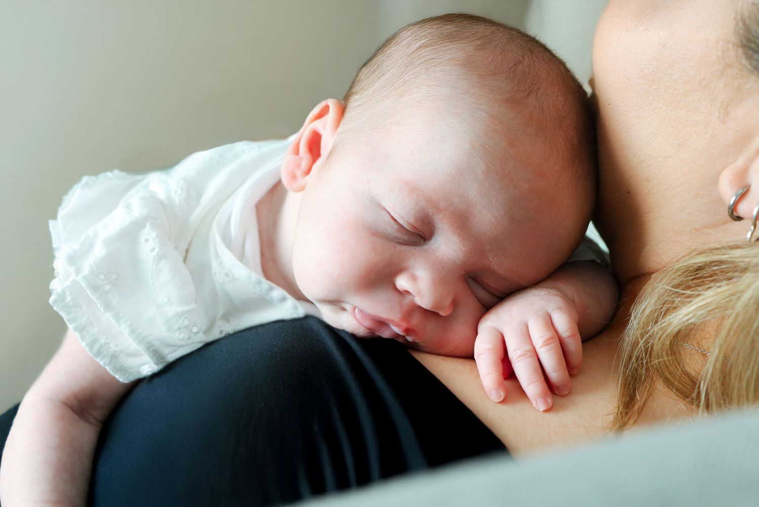 Peaceful sleeping newborn baby swaddled in white blanket with soft natural lighting.