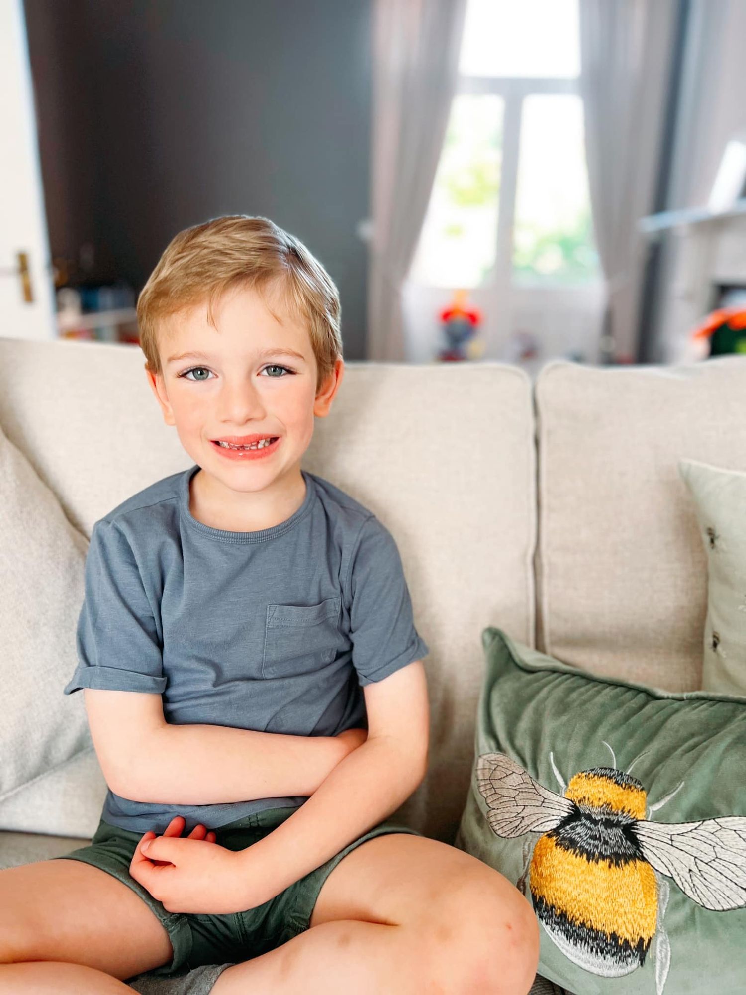 Young child relaxing on a gray couch with a decorative bee pillow.