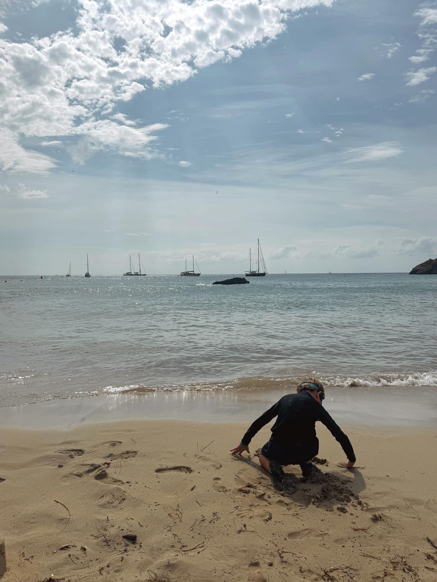 Figure playing in sand at beach with sailboats visible on horizon.