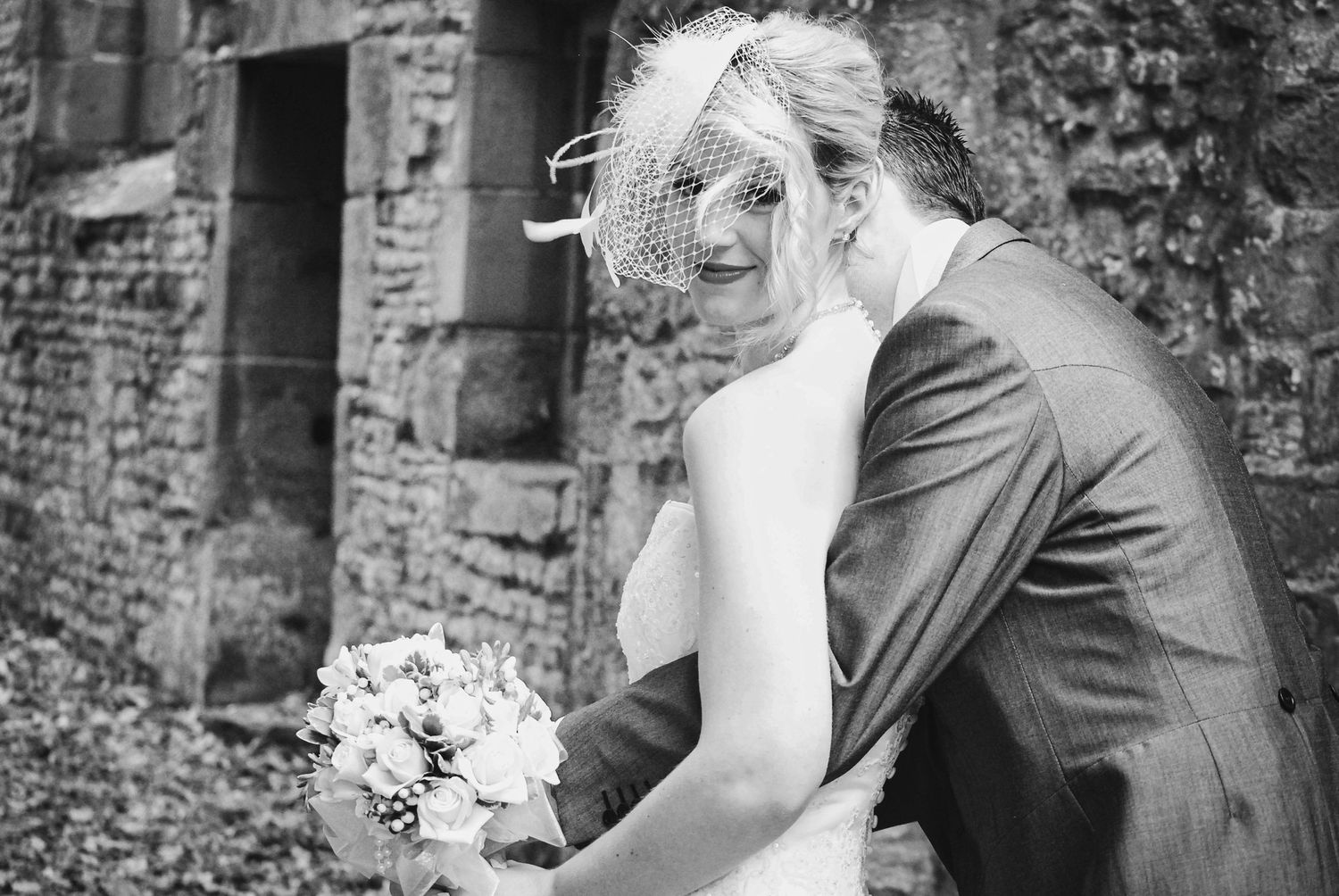 Black and white wedding portrait capturing laughter and joy against rustic brick backdrop.