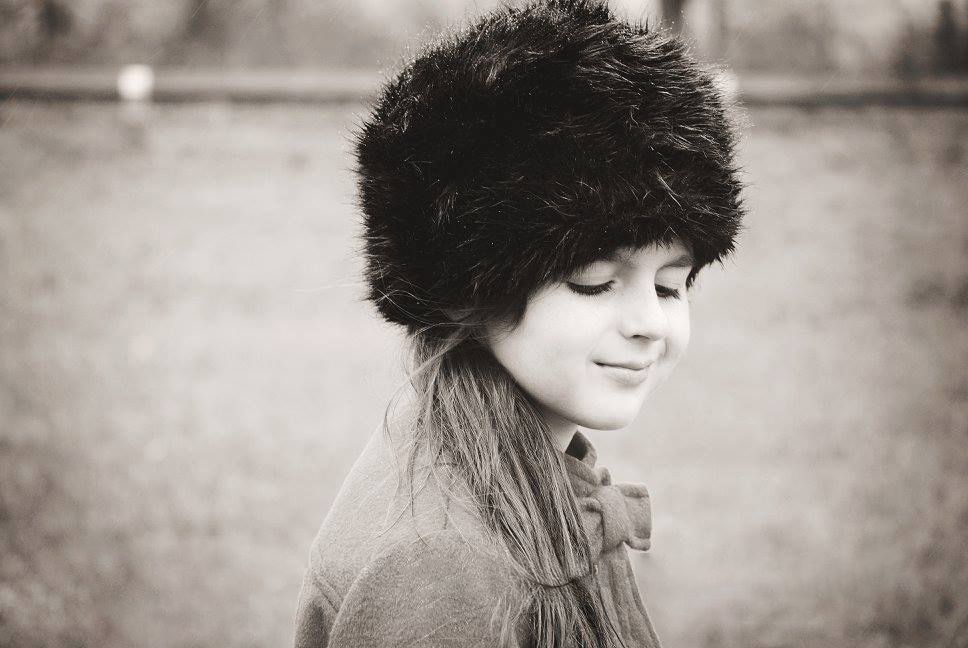 Artistic black and white portrait of someone wearing a plush winter hat with eyes closed.