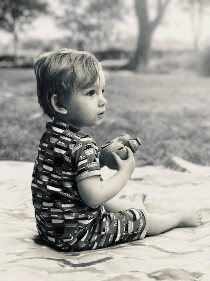 Black and white photo of a small child sitting on a blanket outdoors wearing a patterned outfit.