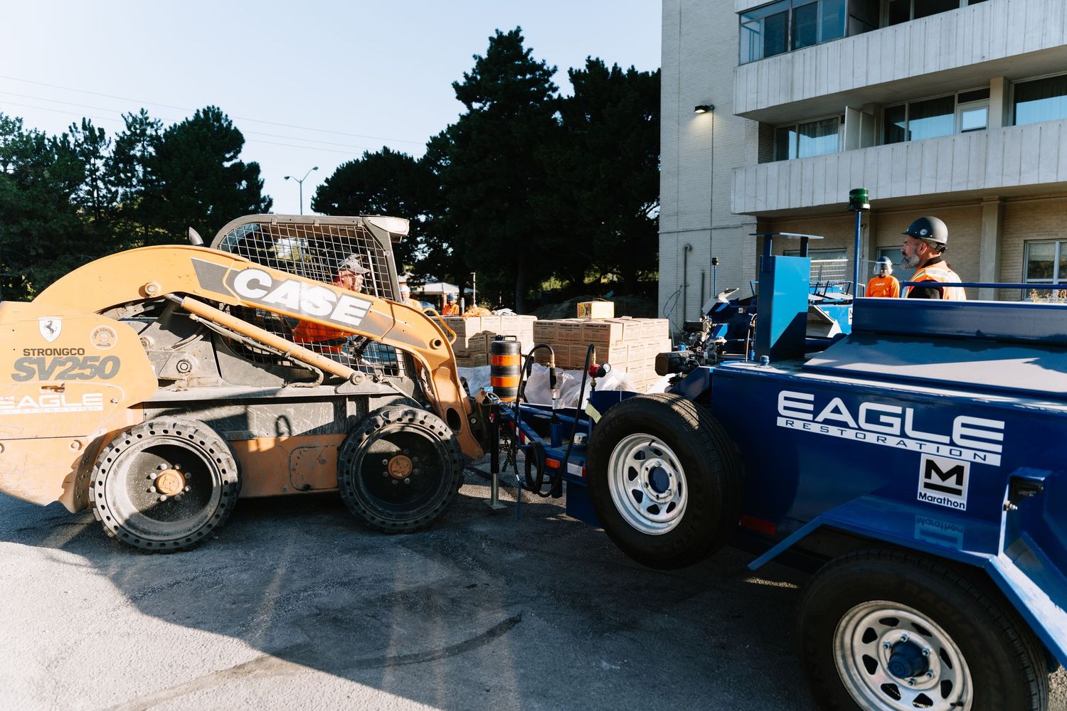 Construction equipment and a blue truck parked outside a building during a loading or unloading operation.