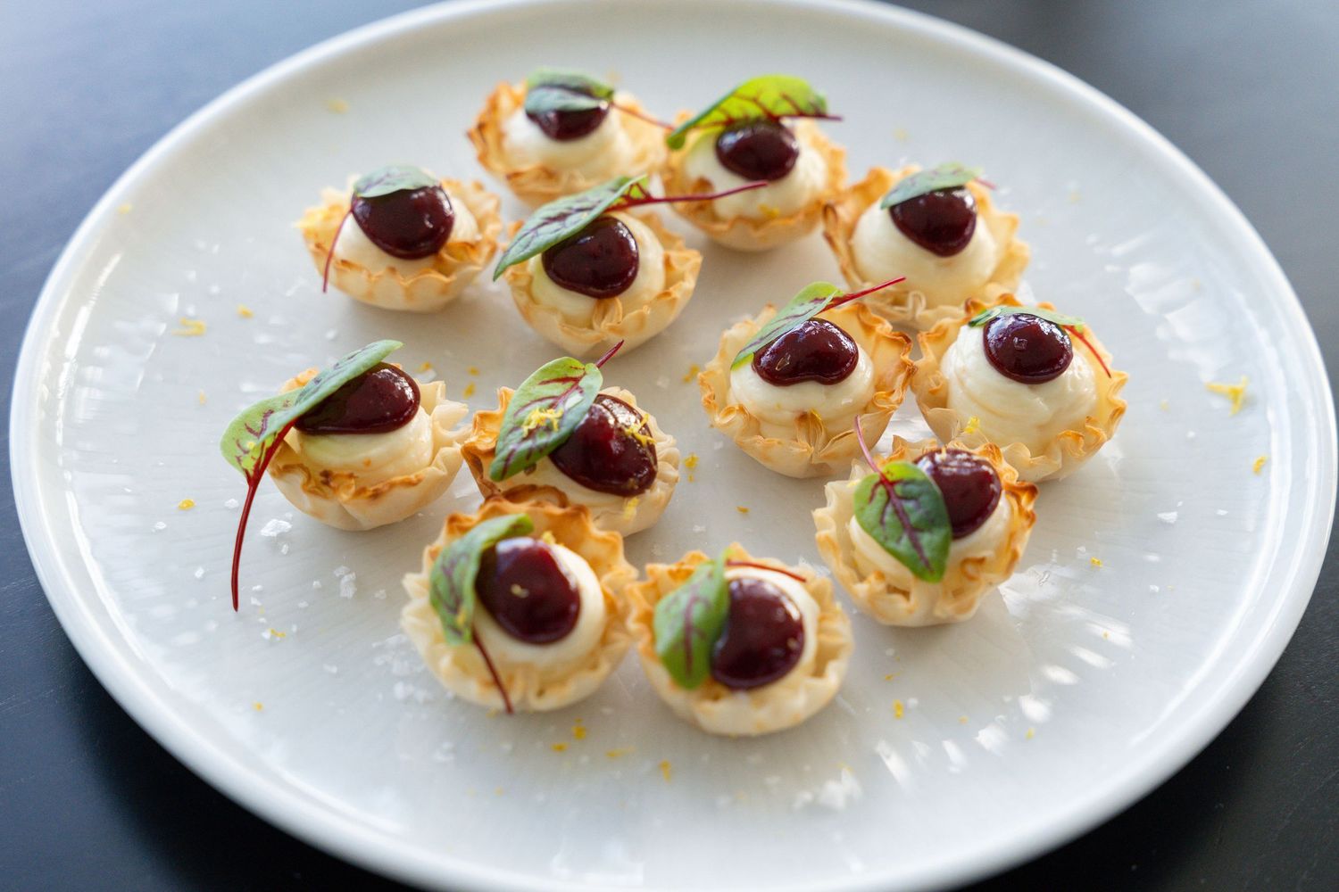Mini phyllo pastry cups filled with creamy goat cheese and topped with cranberries arranged on white plates.