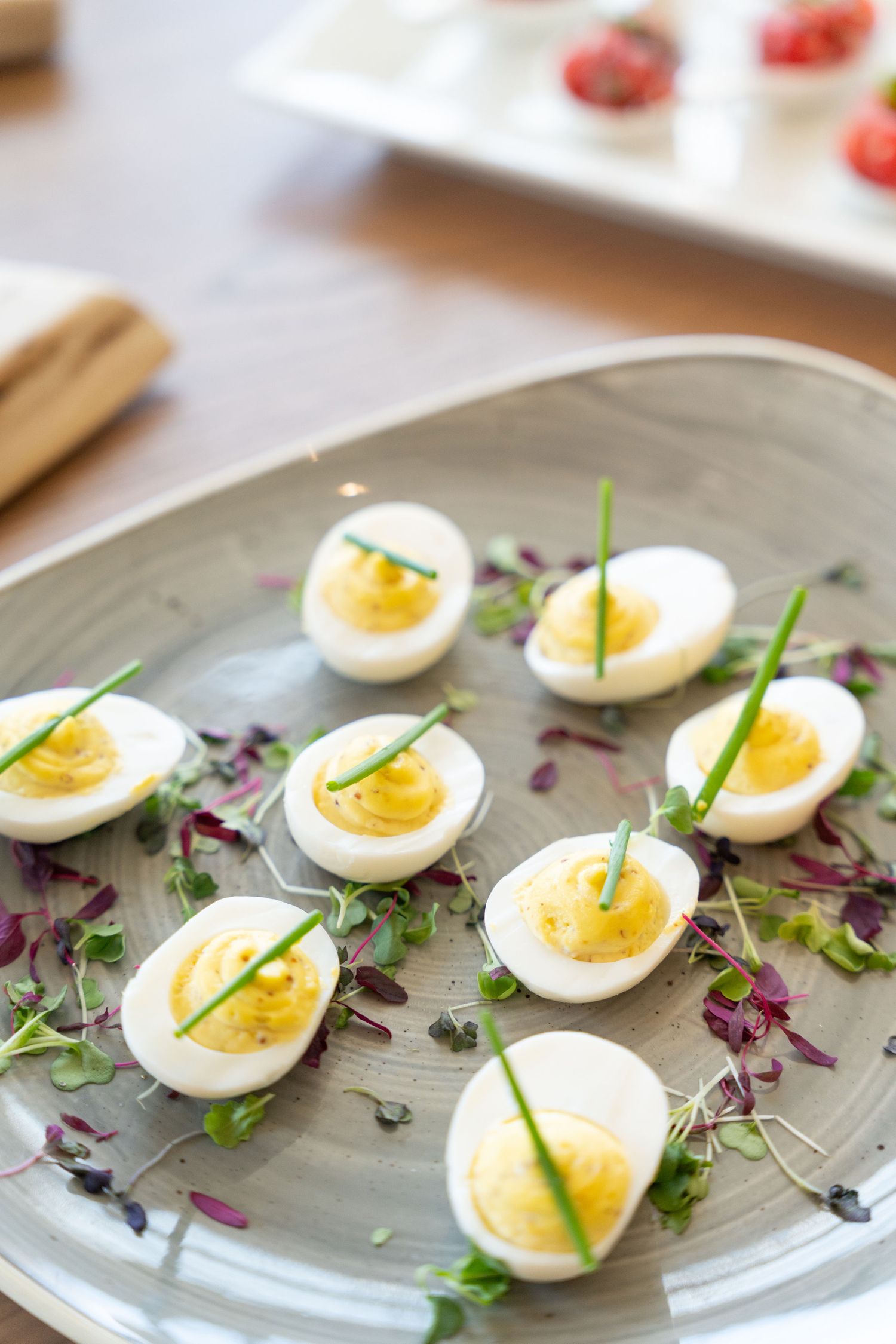Deviled eggs garnished with chives and purple microgreens arranged artfully on a gray plate.