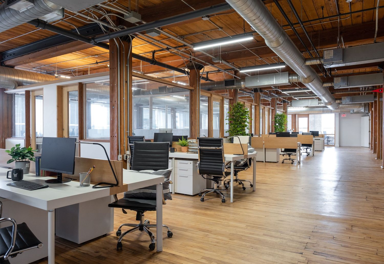 Modern open office space with exposed ceiling, wooden floors, and industrial design elements showcasing collaborative workstations.