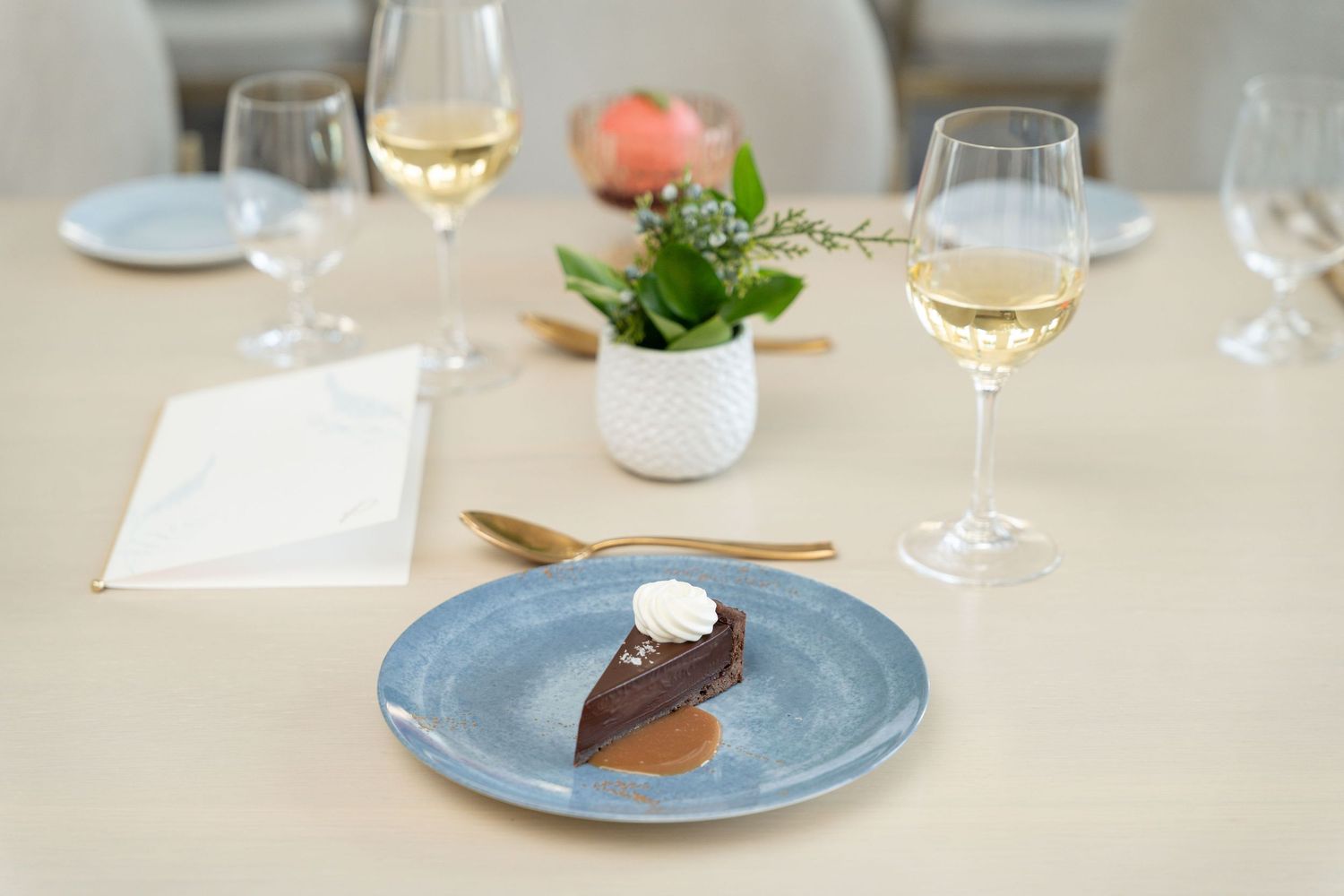 White wine glasses and fine dining plates arranged on a minimalist table setting with natural lighting.