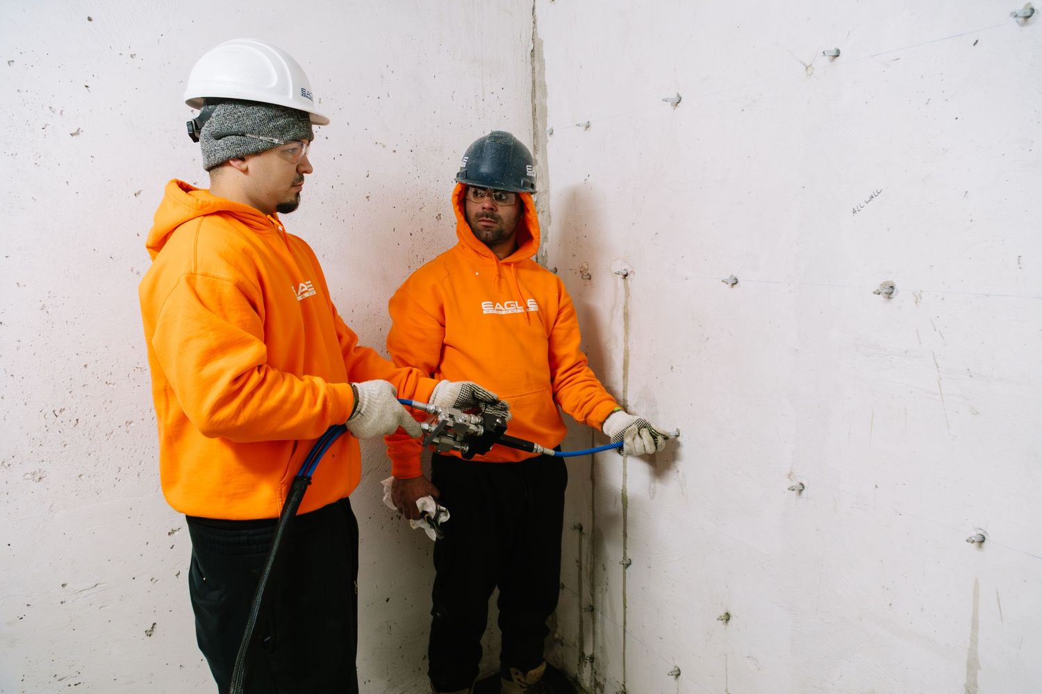Workers in bright orange safety gear install equipment on a concrete wall.