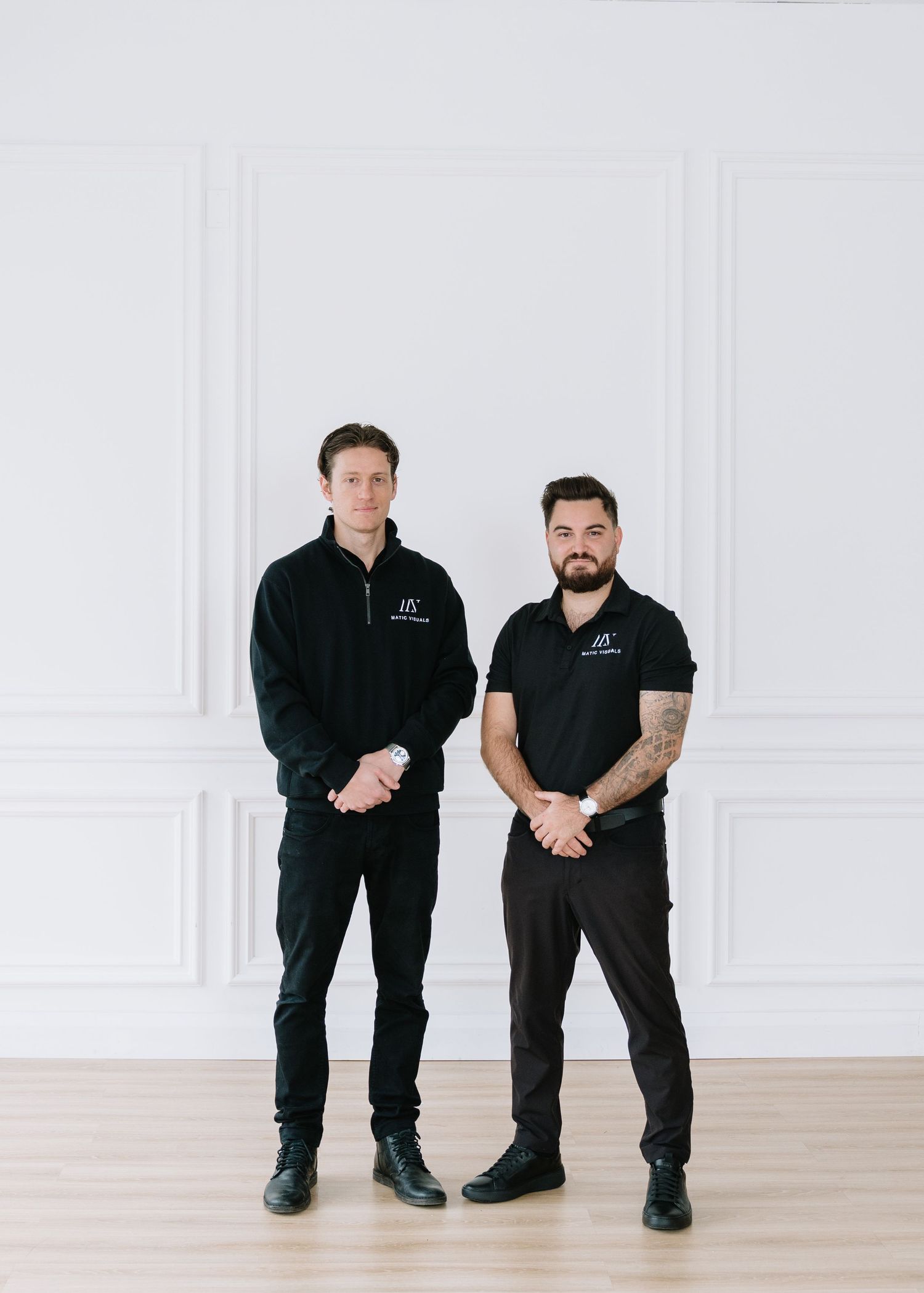 Two men in black uniforms demonstrate different stages of kneeling positions in a bright white room with hardwood floors.