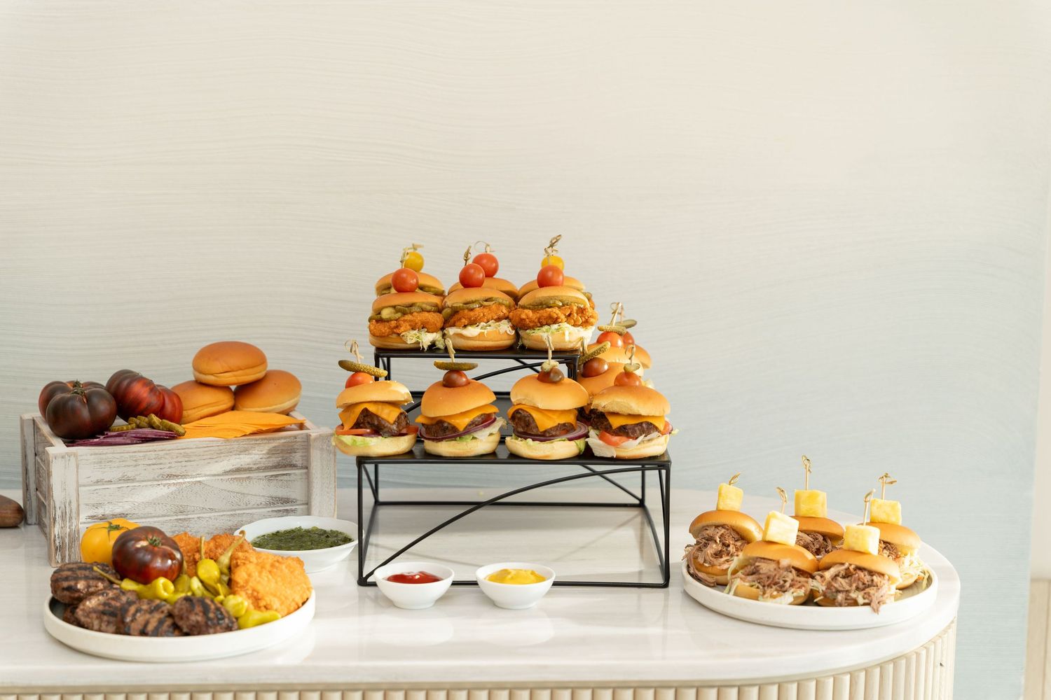 Tiered display of gourmet sliders and appetizers arranged on white serving platters.