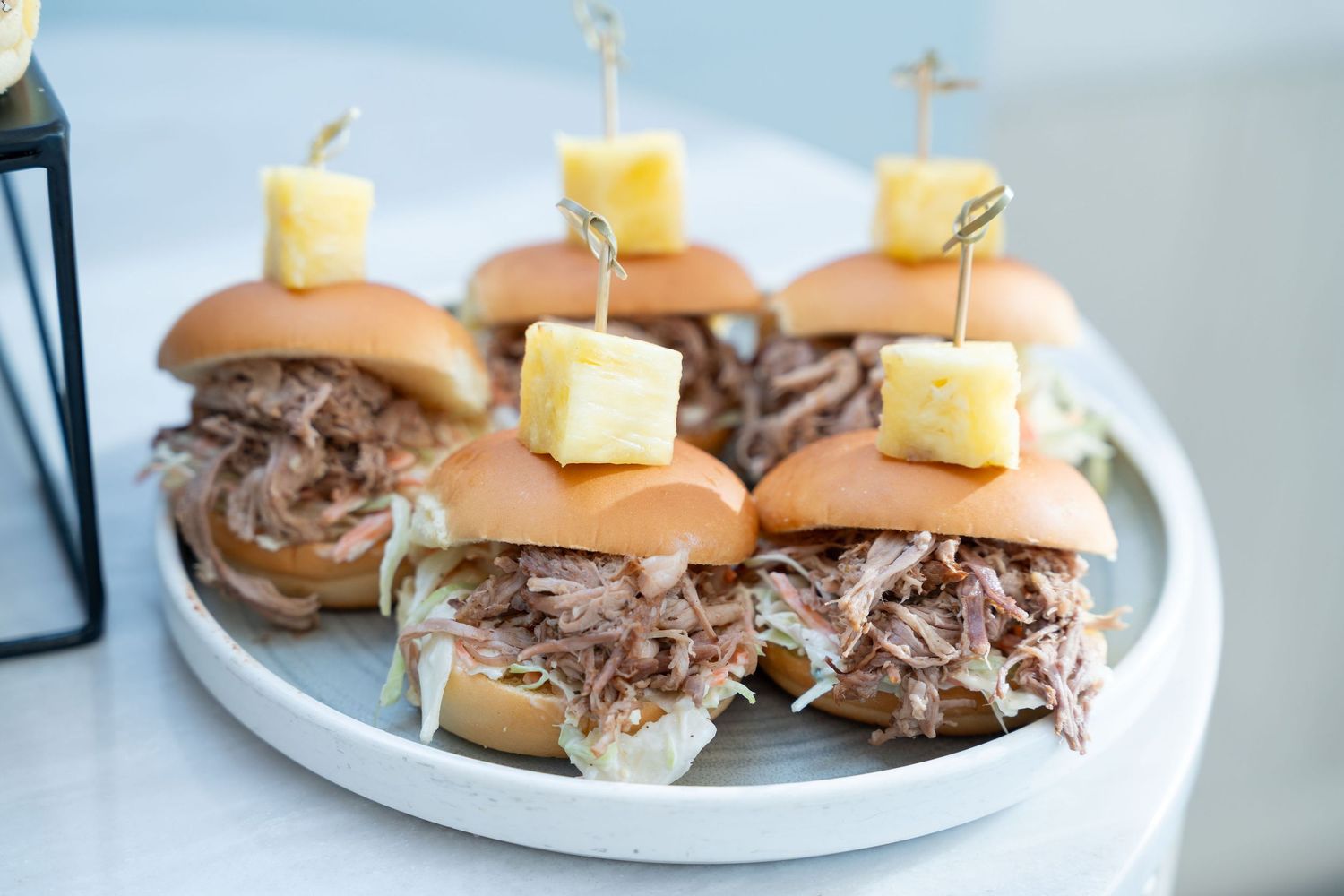 Pulled pork sliders with melted cheese squares served on white plates in a restaurant setting.