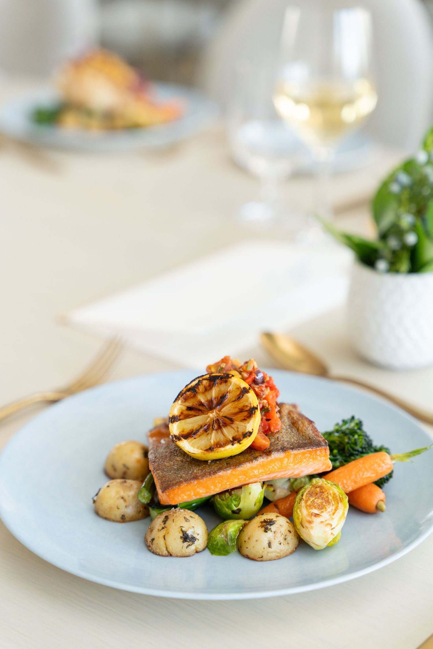 Elegant plated salmon dish with roasted vegetables and grilled lemon garnish served on white plates.