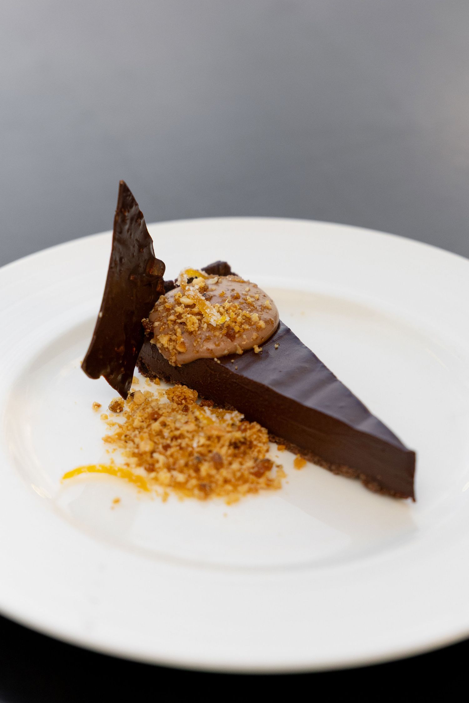 Modern dessert presentation with dark chocolate shards and golden crumble on a white plate.