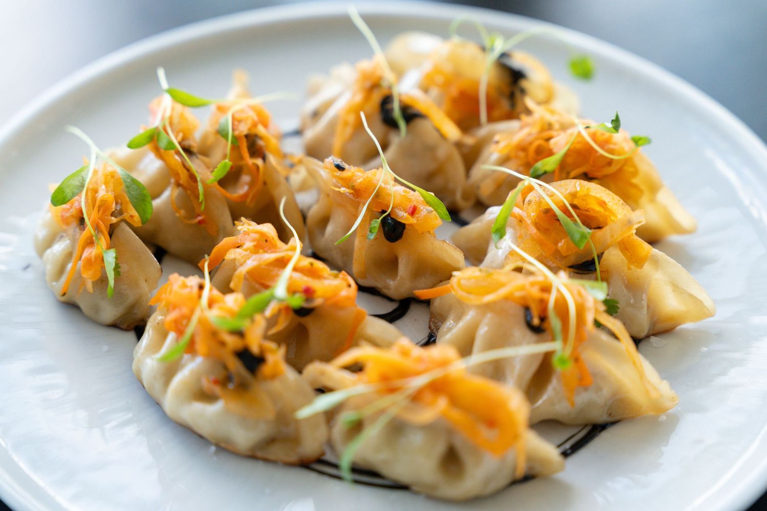 Steamed dumplings topped with shredded carrots and fresh chives arranged on a white plate.
