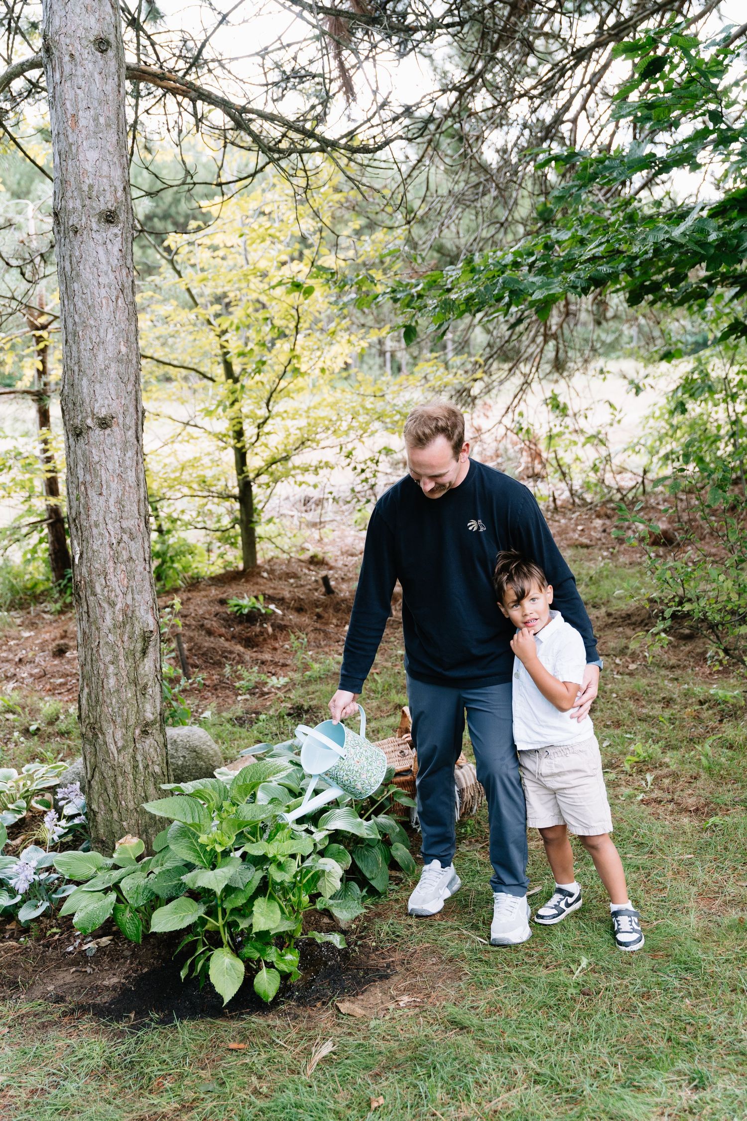 Adult and child looking at plants in wooded garden setting while wearing casual clothing.