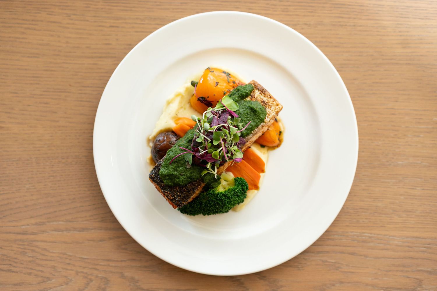 A sequence of white plates on a wooden table showing progressively eaten portions of broccoli and salmon.
