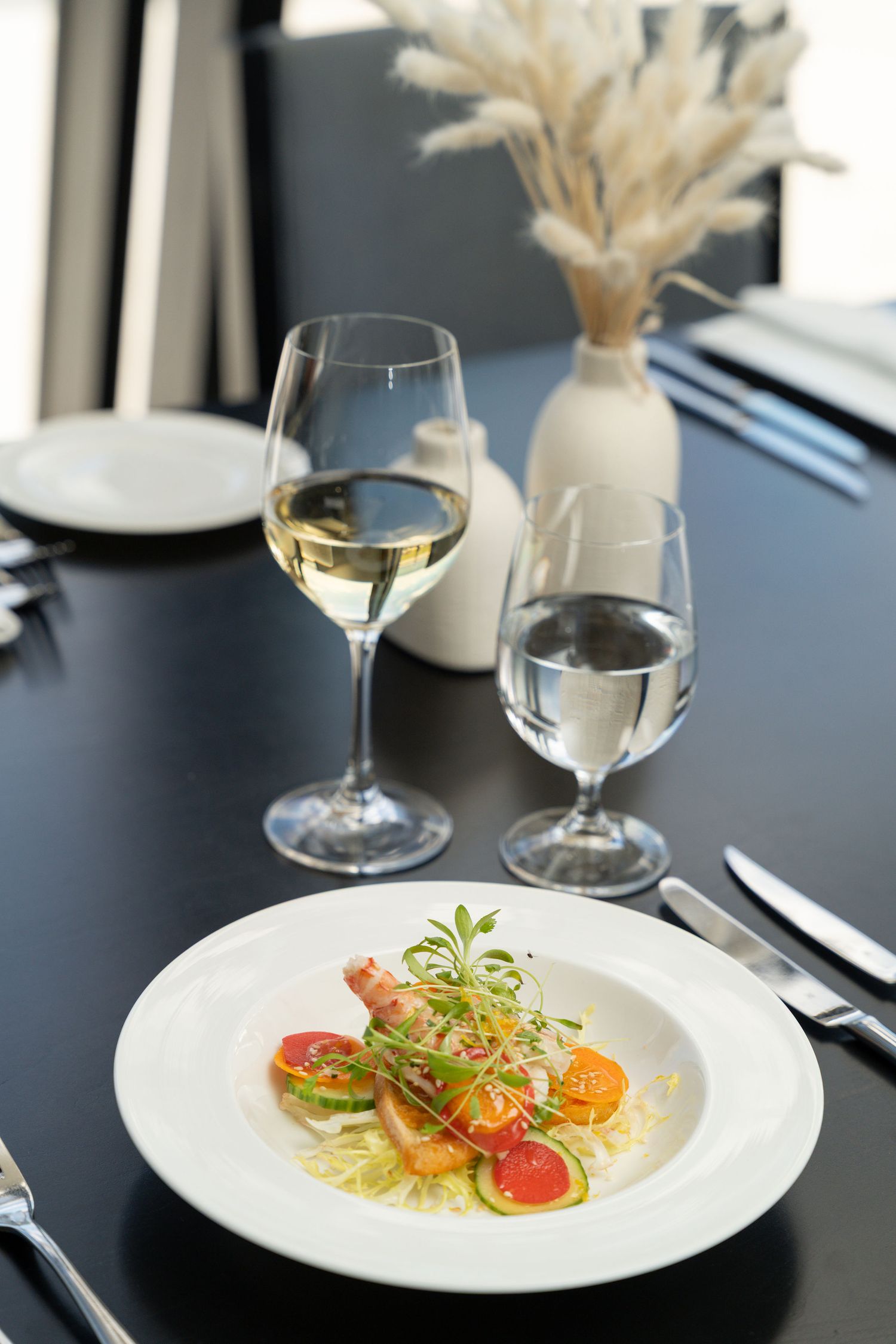 Fine dining table setting with white wine glasses and decorative wheat stalks alongside plated appetizers.