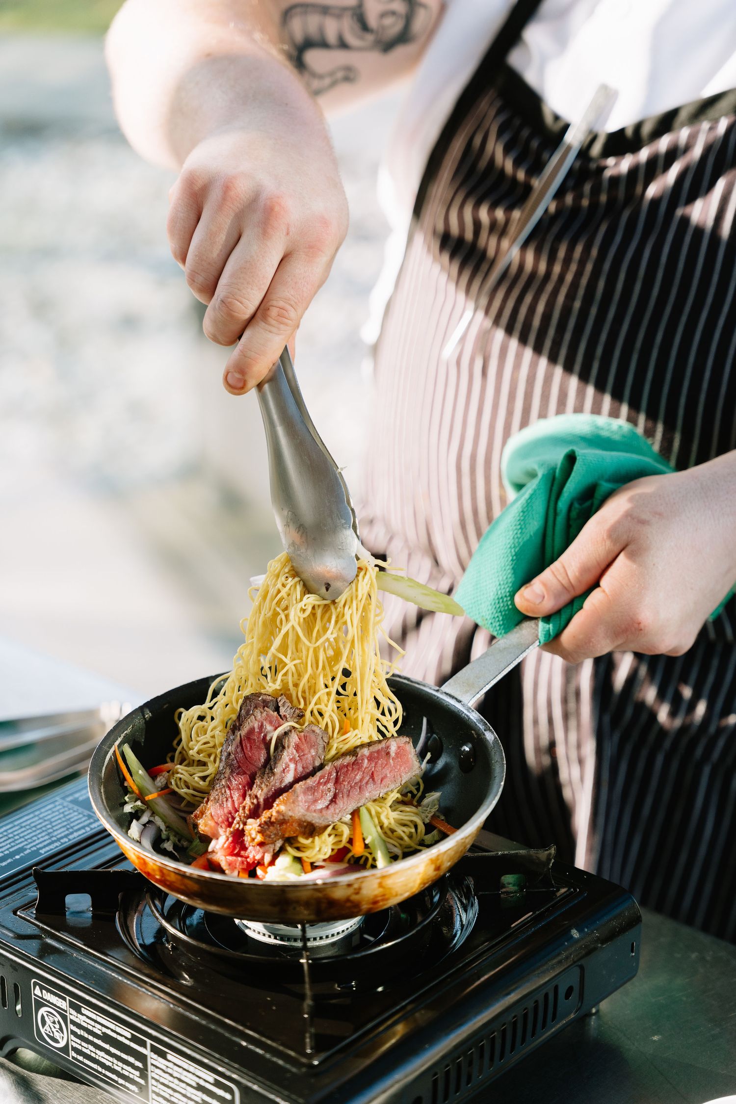 Chef cooking and plating pasta dish in restaurant kitchen using green protective gloves.