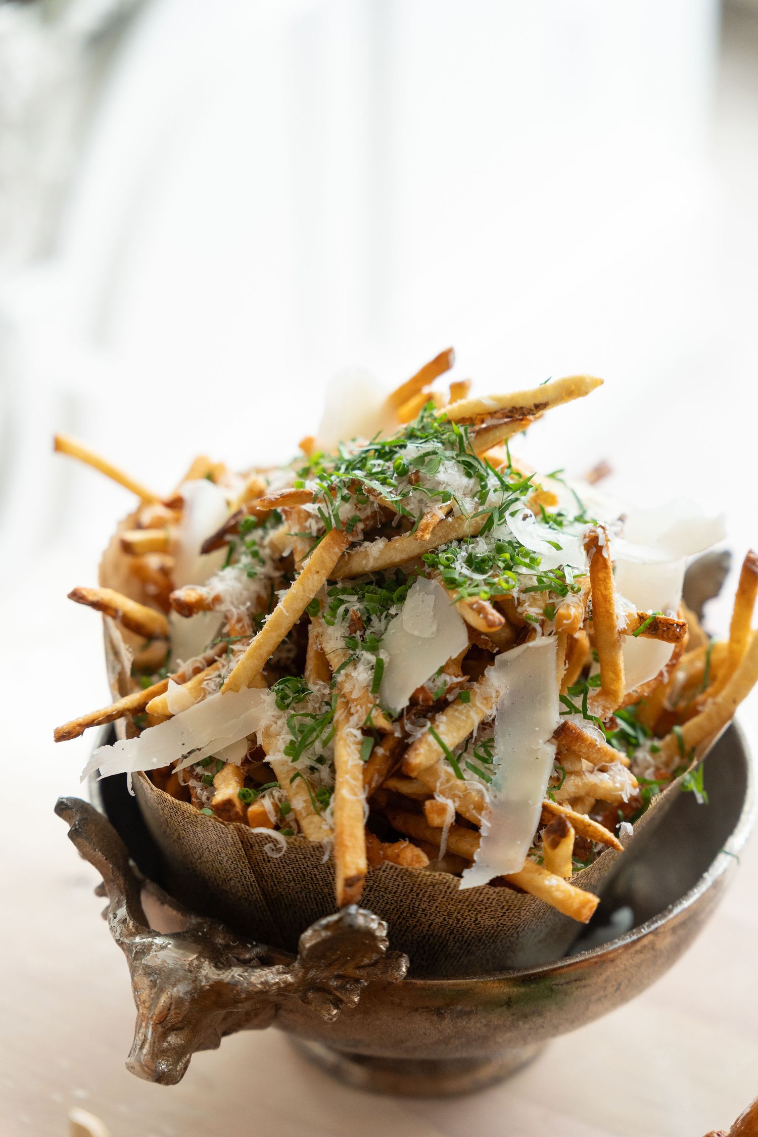 Crispy french fries topped with fresh herbs and shaved parmesan cheese served in dark ceramic bowls.