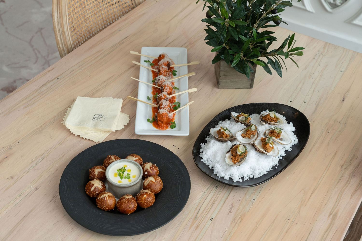 Overhead view of Asian fusion dishes including meatballs and rice served on black plates on a wooden table with greenery.