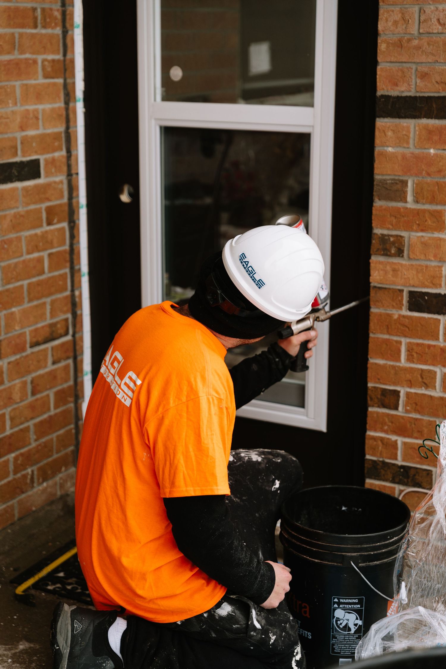 Worker in bright orange shirt performs maintenance tasks near windows of brick building.