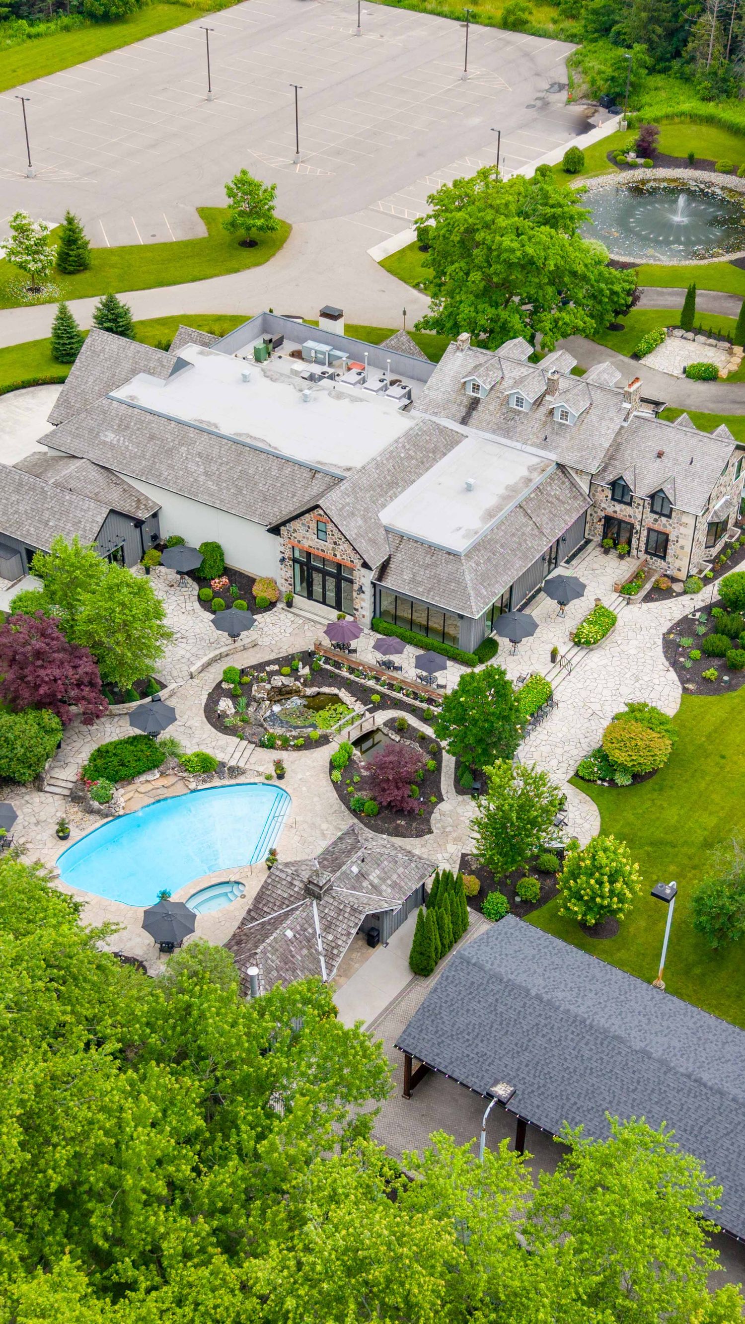 Aerial view of a luxury estate with a pool, manicured gardens, stone mansion, and decorative fountain.