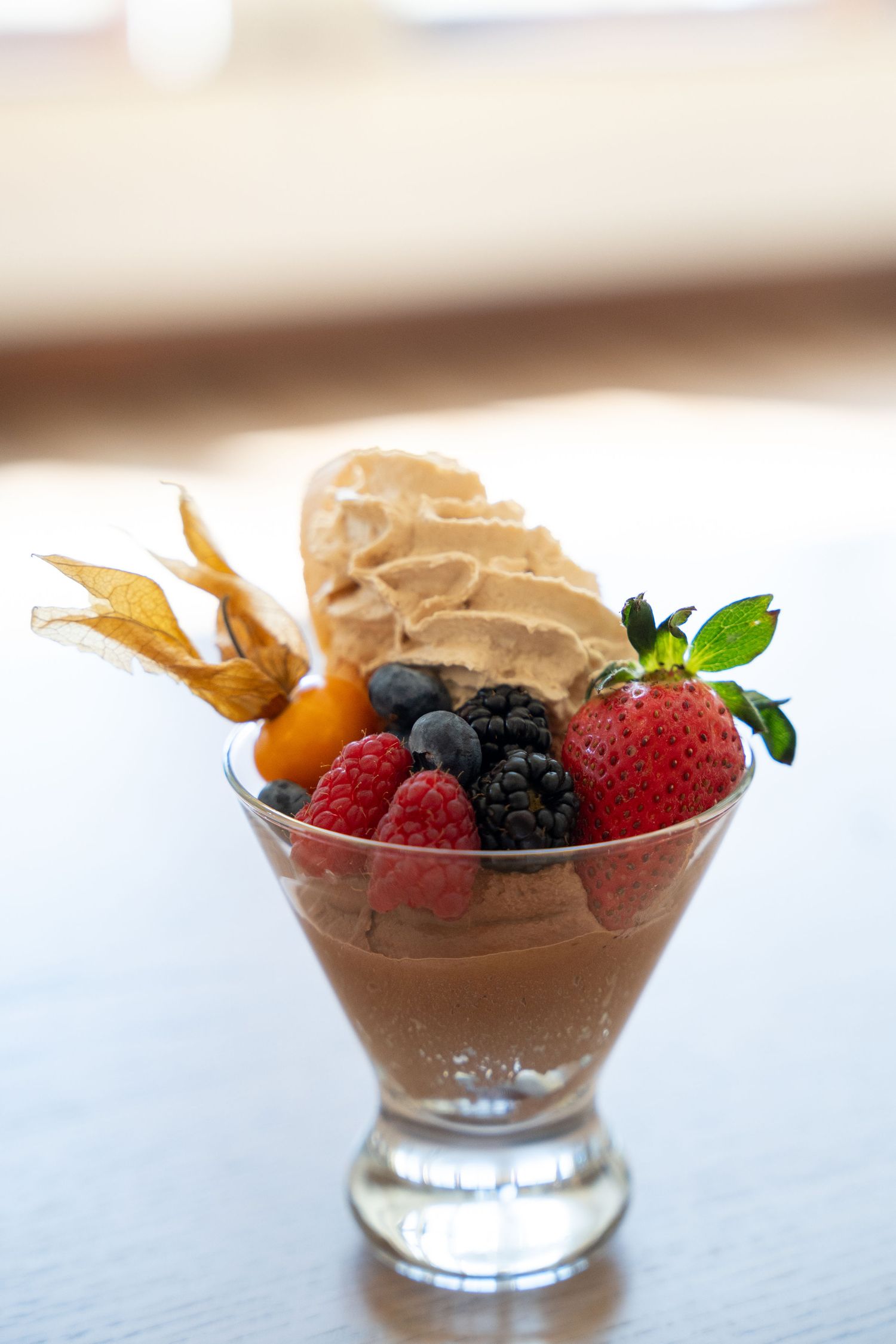 A decadent chocolate mousse dessert topped with fresh berries and garnished with golden physalis in glass bowls.