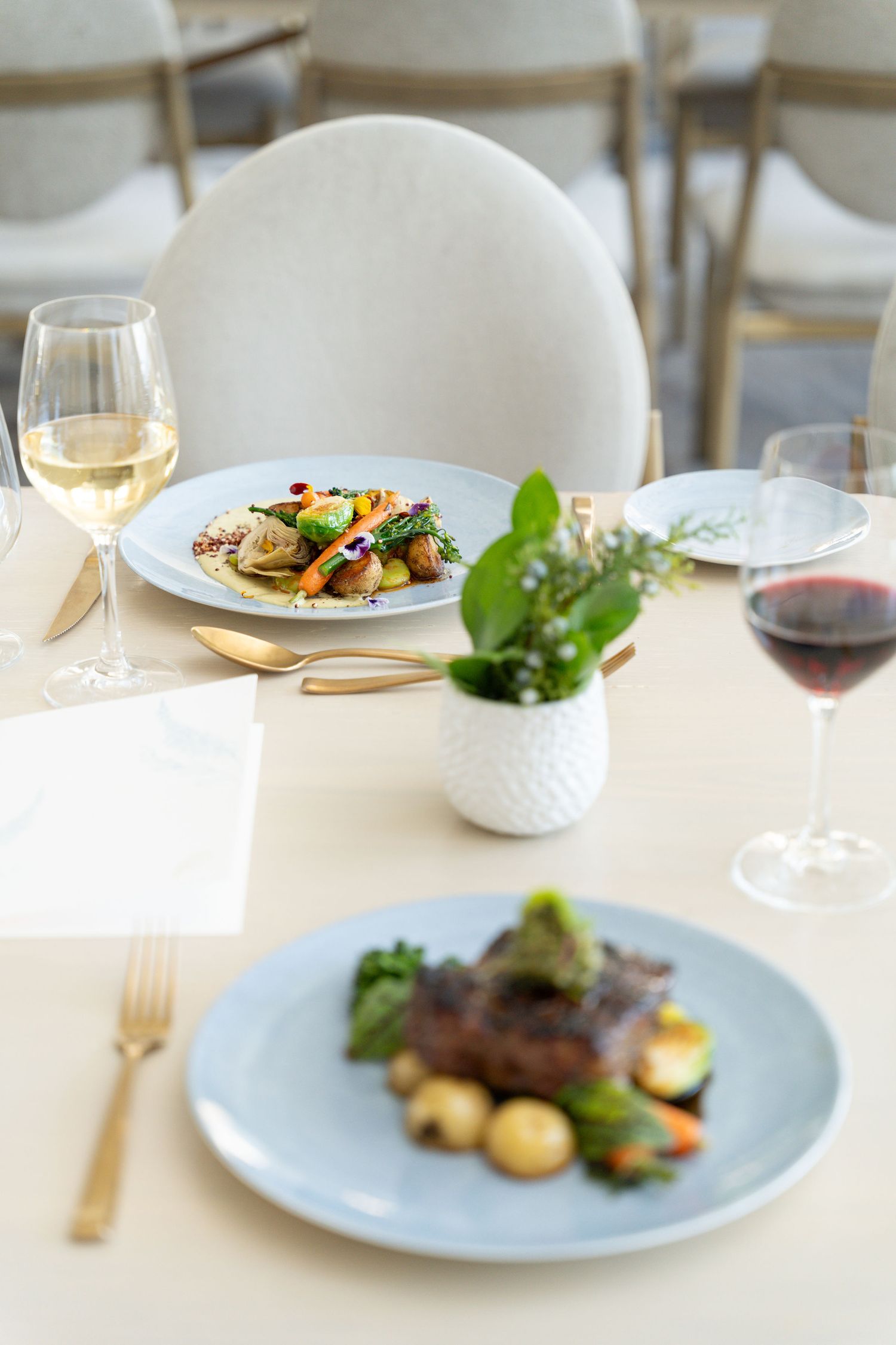 Elegant restaurant table setting with plated meals, wine glasses, and decorative plant centerpiece.