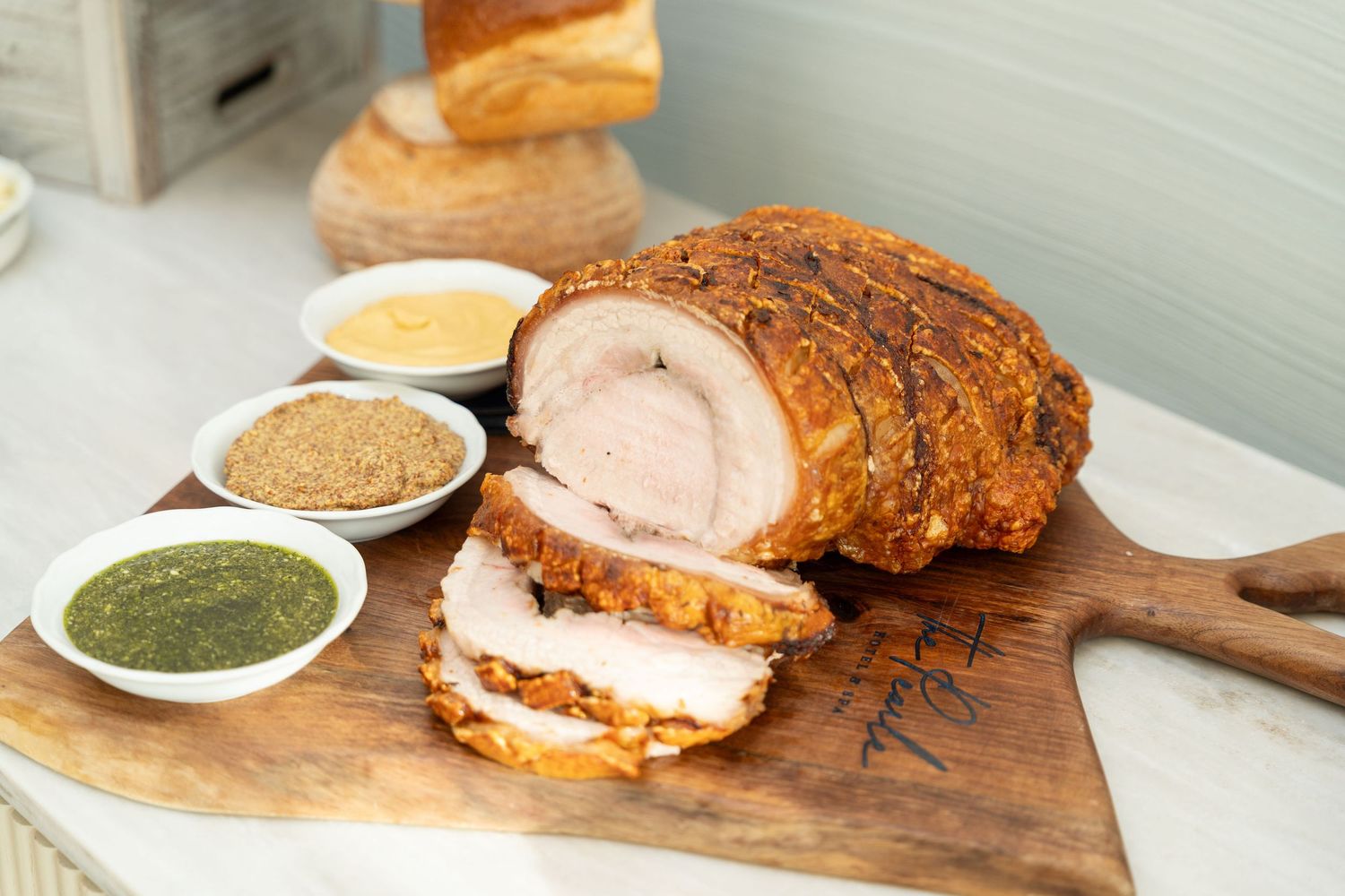 Carved porchetta on wooden board served with three dipping sauces in small bowls.