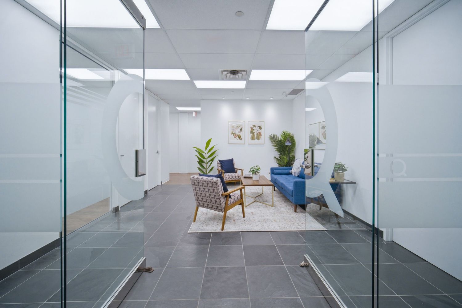 Modern office hallway with glass walls, grey flooring, and bright fluorescent lighting creates a sleek corporate environment.