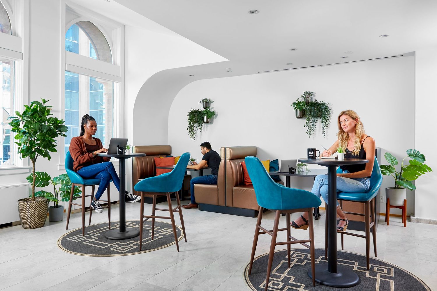 Bright minimalist office lounge featuring modern furniture, plants, and white interior design.