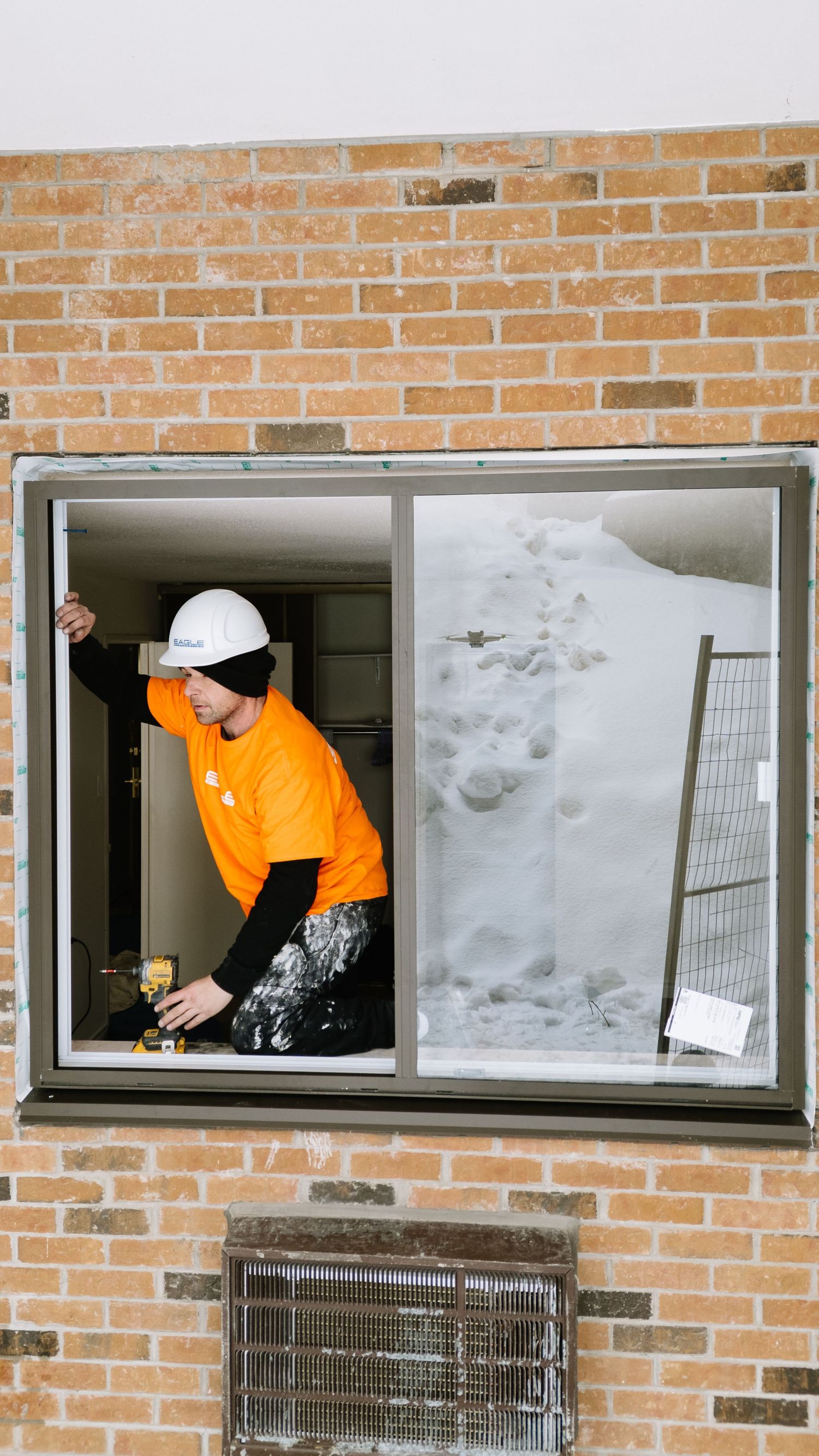 Workers in orange safety vests perform maintenance through open windows of a brick building.