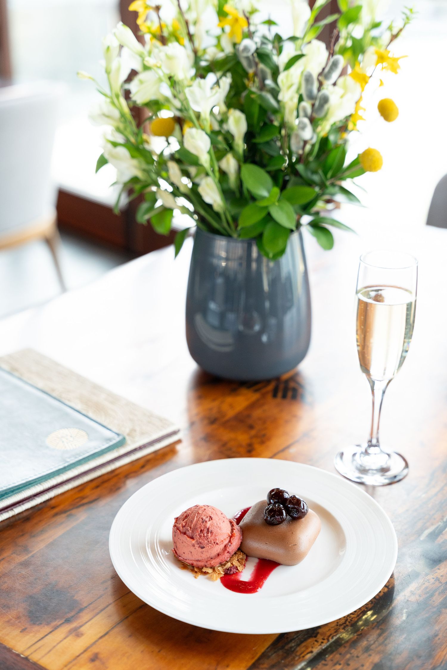 Dessert plates with chocolate mousse and sorbet garnished with fresh flowers and berries on a wooden surface.